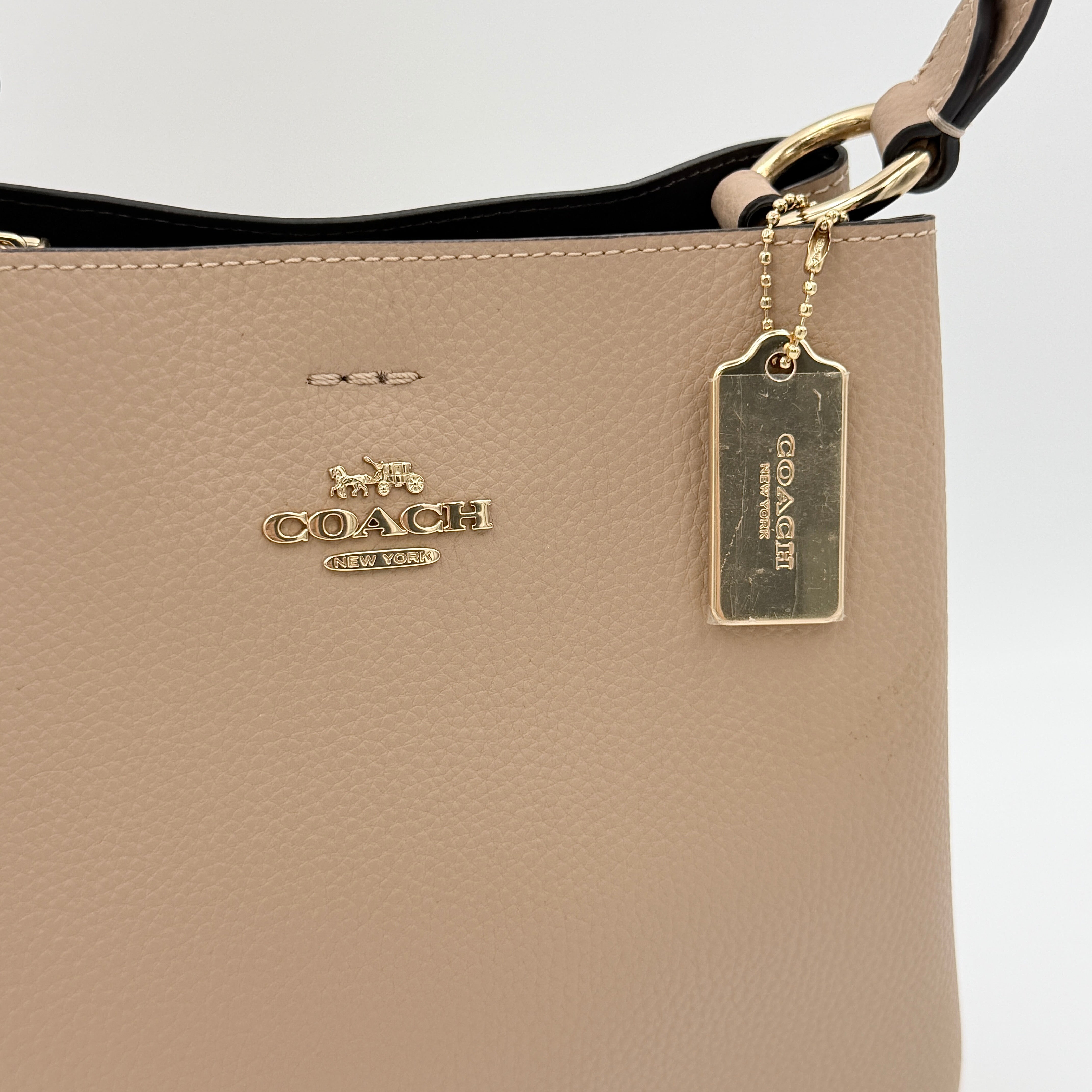 Coach Town Bucket Bag in taupe pebbled leather with gold-tone hardware and Coach hangtag, shown against a white background.