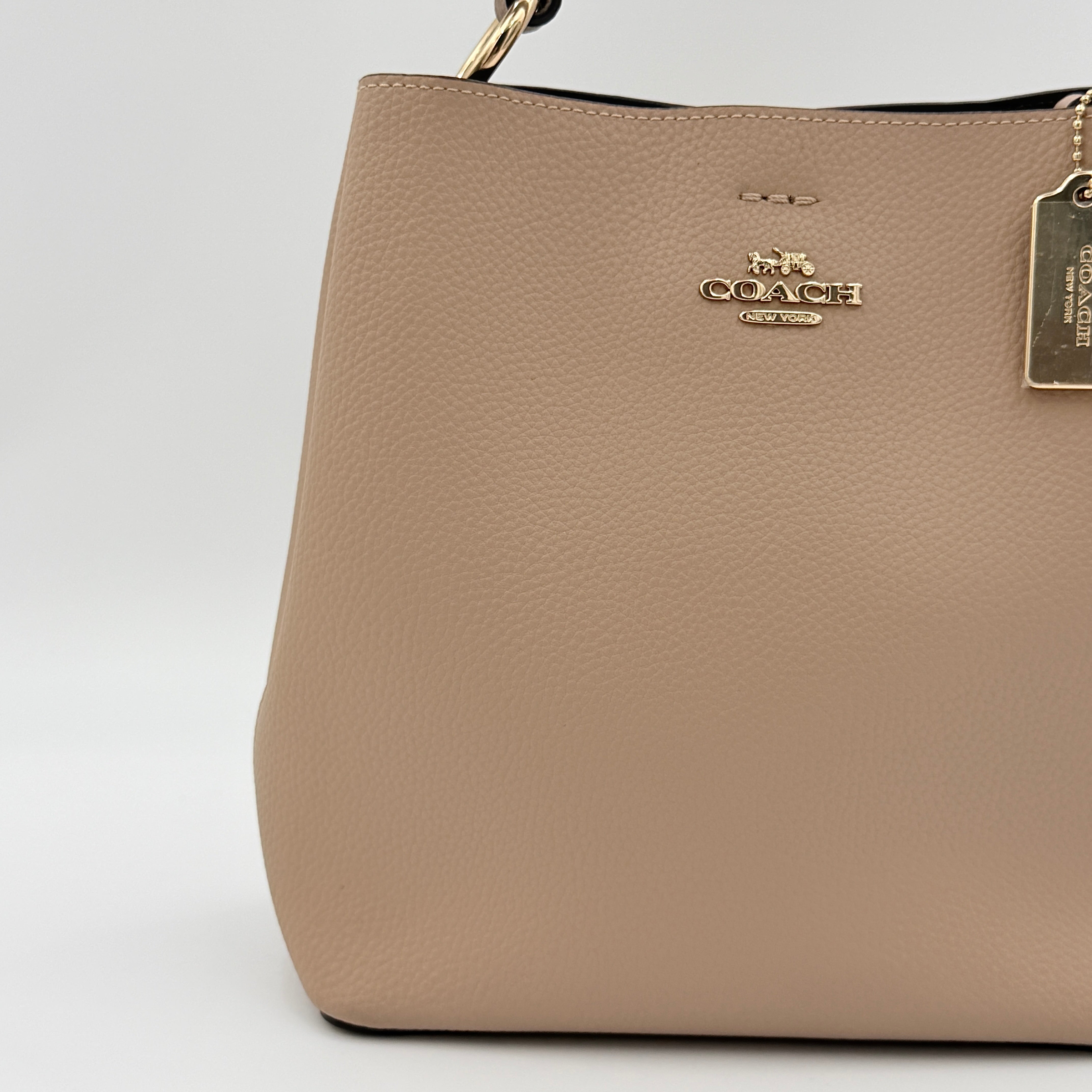 Coach Town Bucket Bag in taupe pebbled leather with gold-tone hardware and Coach hangtag, shown against a white background.