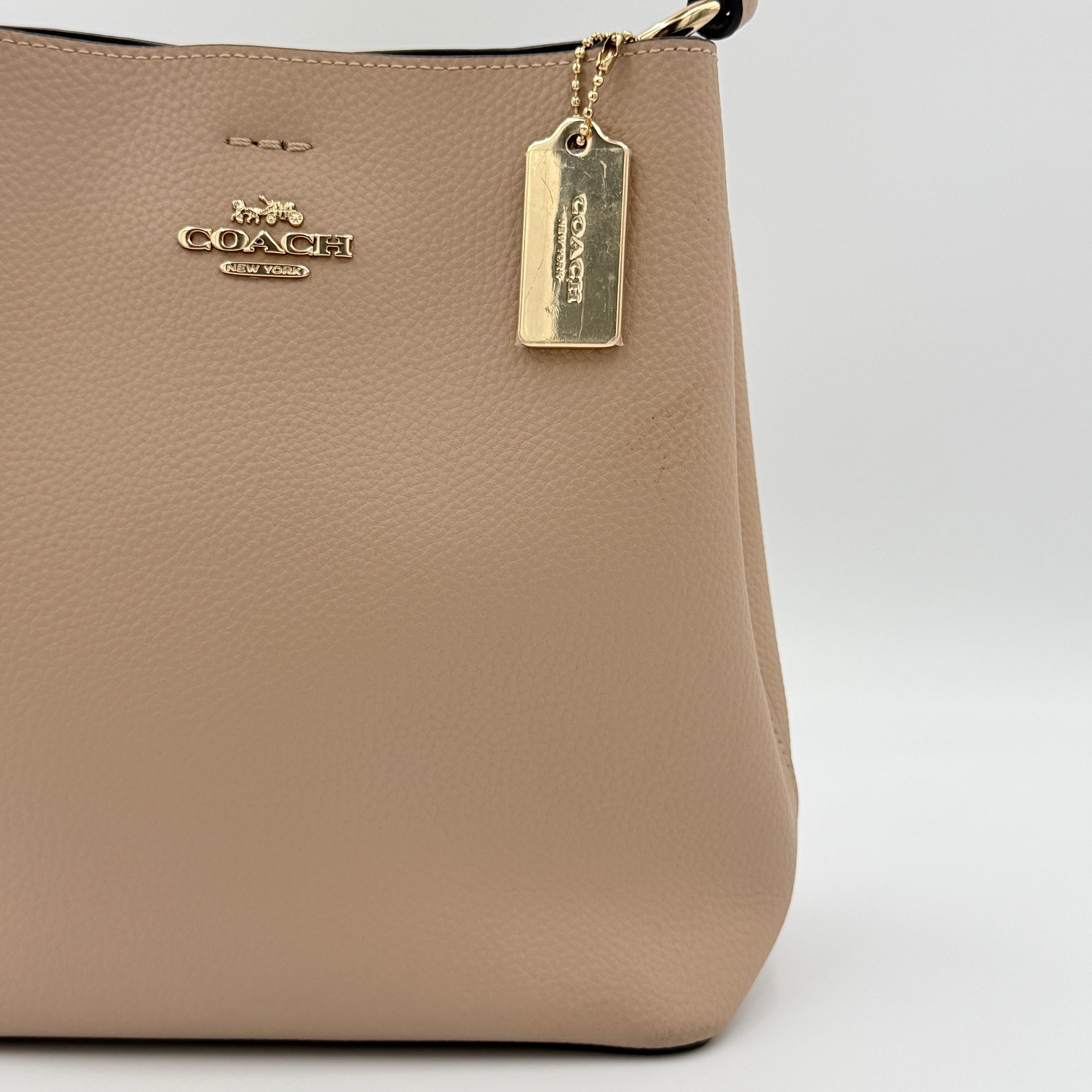 Coach Town Bucket Bag in taupe pebbled leather with gold-tone hardware and Coach hangtag, shown against a white background.