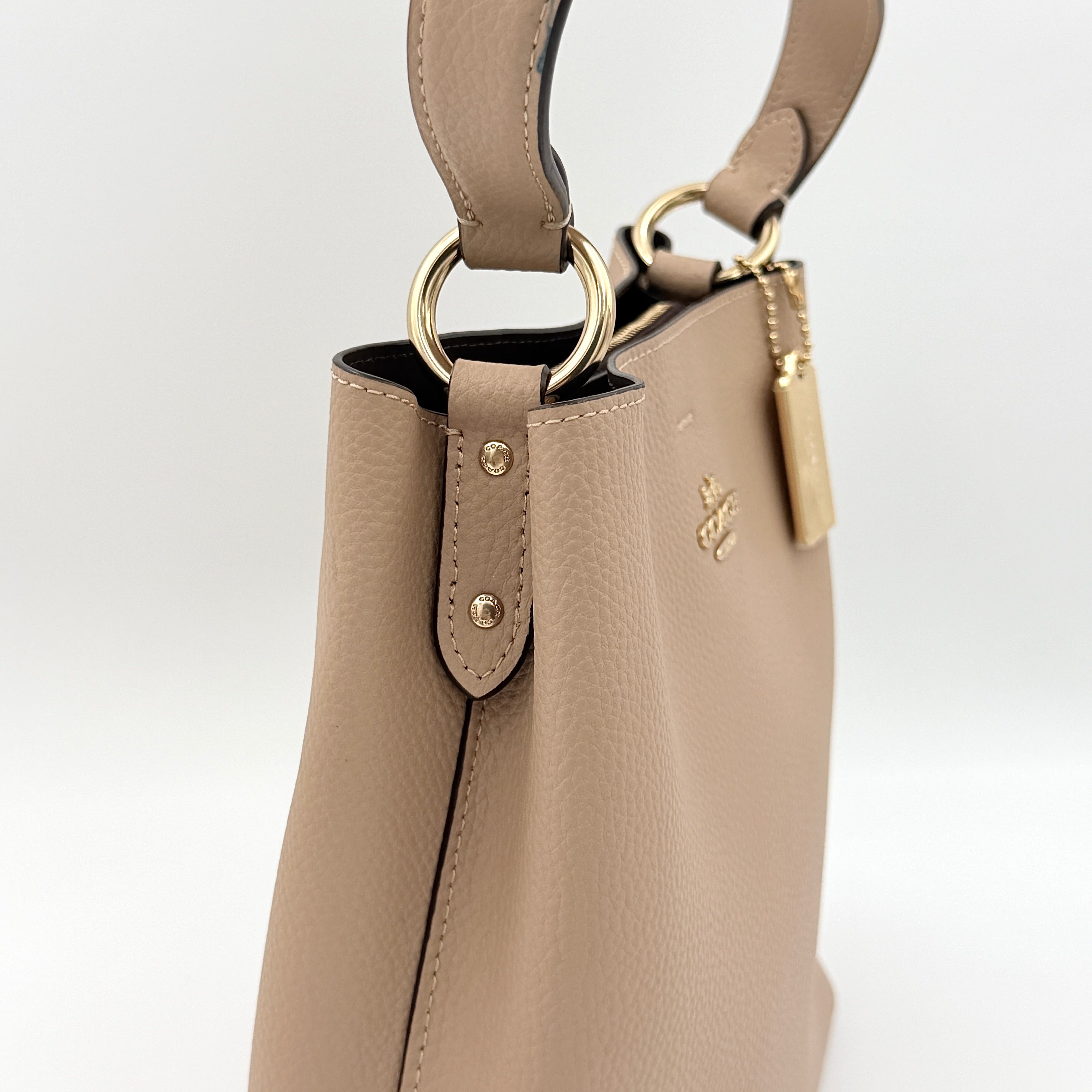 Coach Town Bucket Bag in taupe pebbled leather with gold-tone hardware and Coach hangtag, shown against a white background.