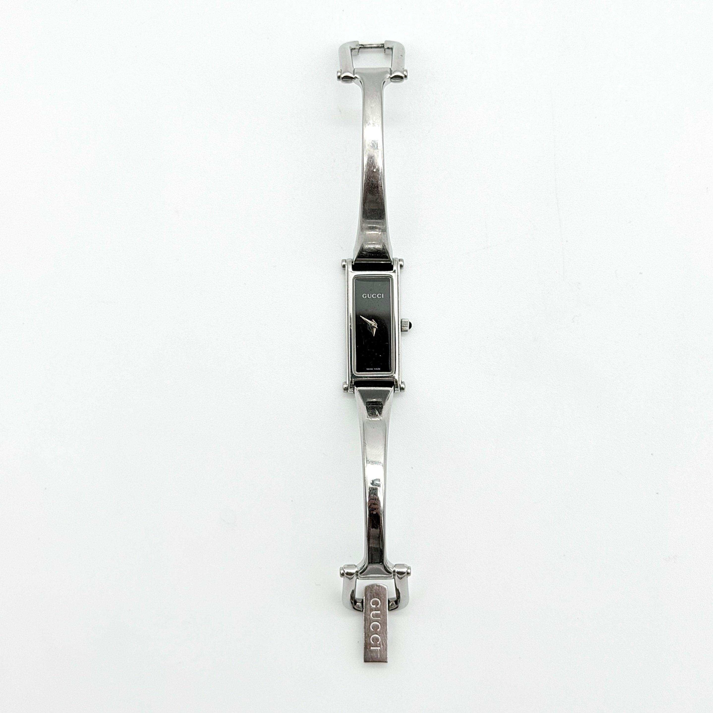 Gucci 1500L black dial bangle watch with stainless steel bracelet, photographed on a clear display stand.
