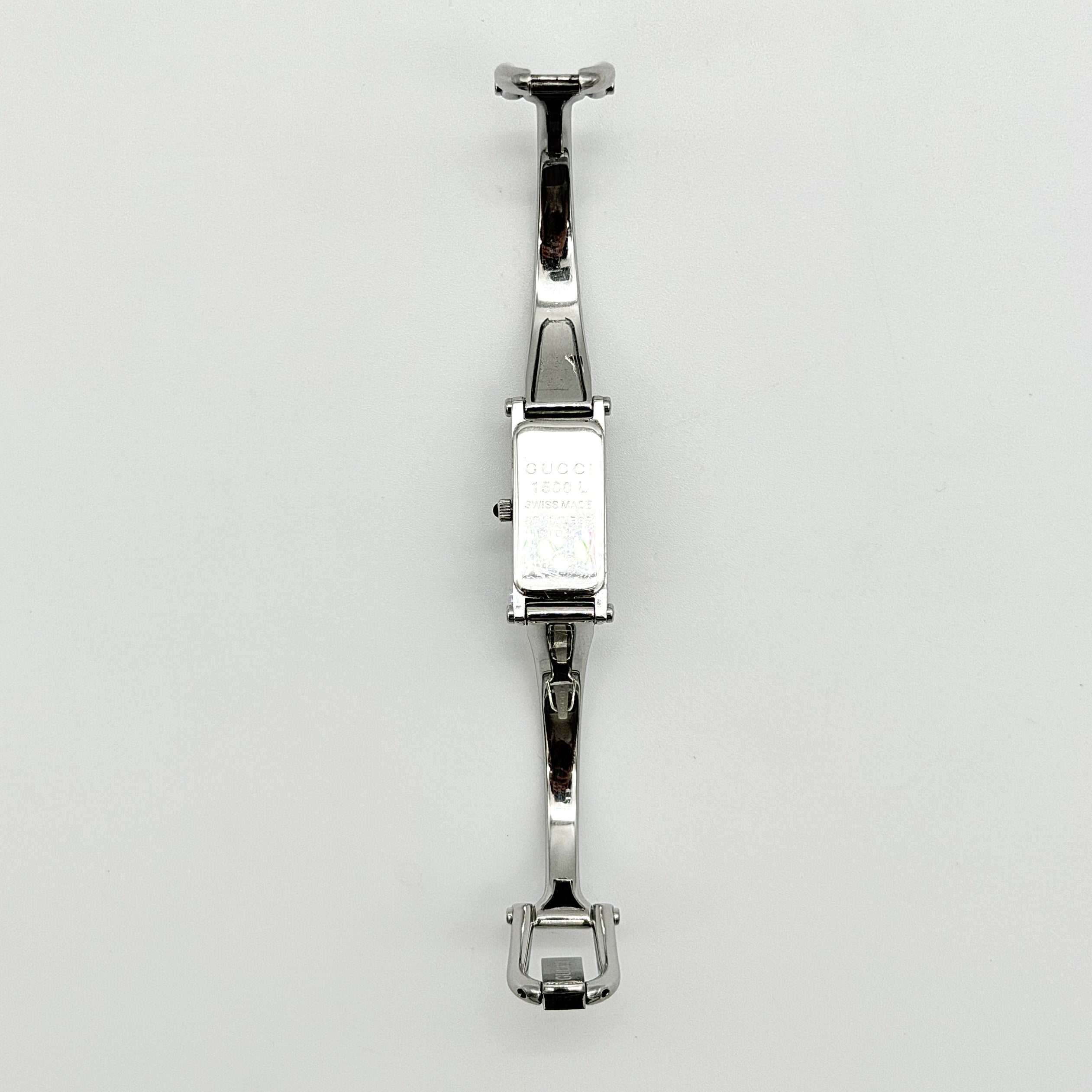 Gucci 1500L black dial bangle watch with stainless steel bracelet, photographed on a clear display stand.
