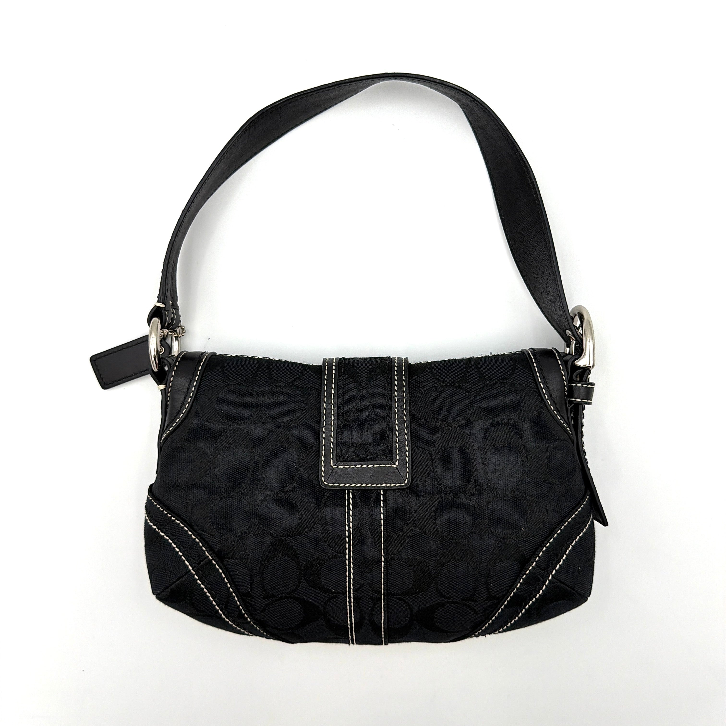 Coach black Signature Soho shoulder bag with oversized silver buckle, cream contrast stitching, and monogram jacquard canvas backdrop.