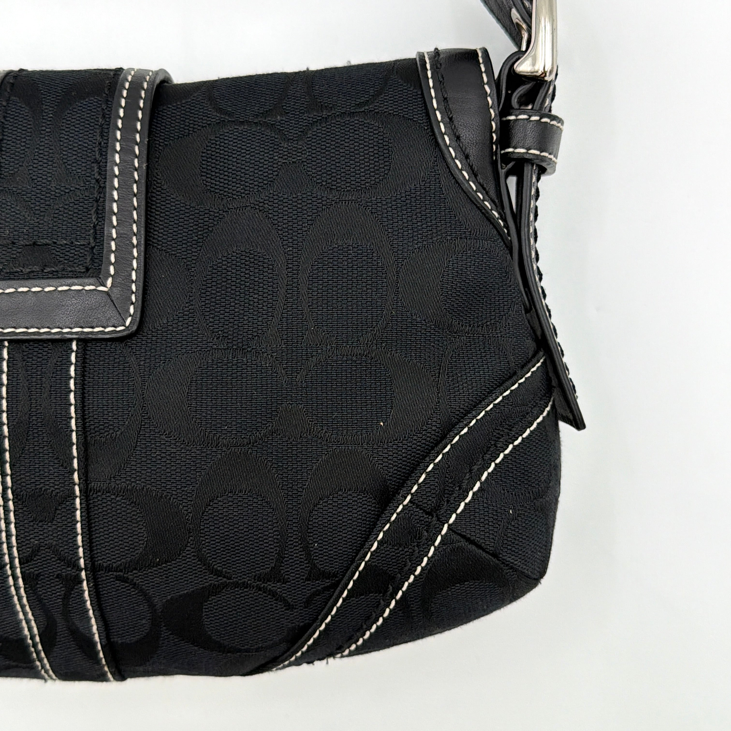 Coach black Signature Soho shoulder bag with oversized silver buckle, cream contrast stitching, and monogram jacquard canvas backdrop.