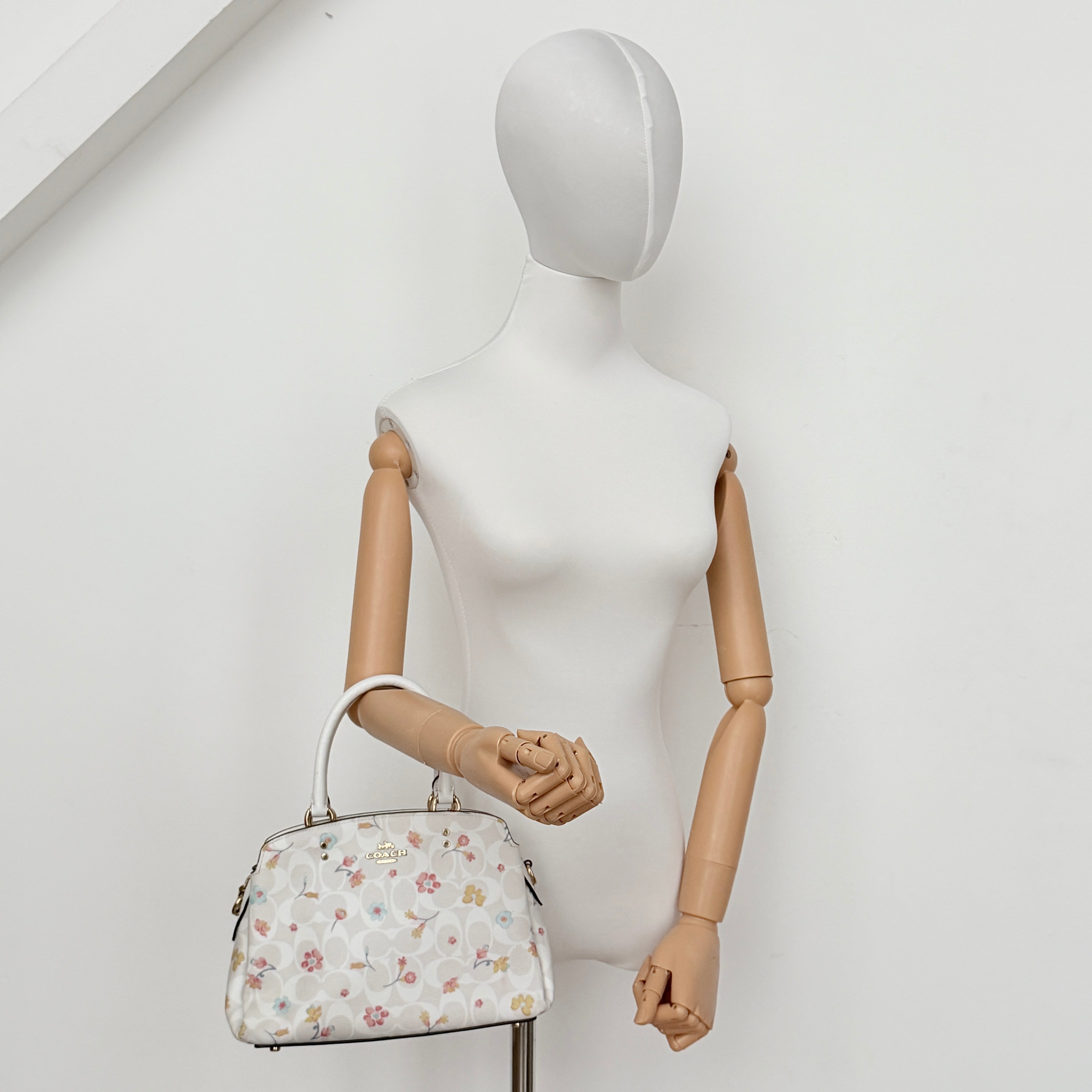 Coach 2Way Signature Lillie Carryall in white canvas with gold hardware and multicolour floral print, accompanied by a detachable white shoulder strap.