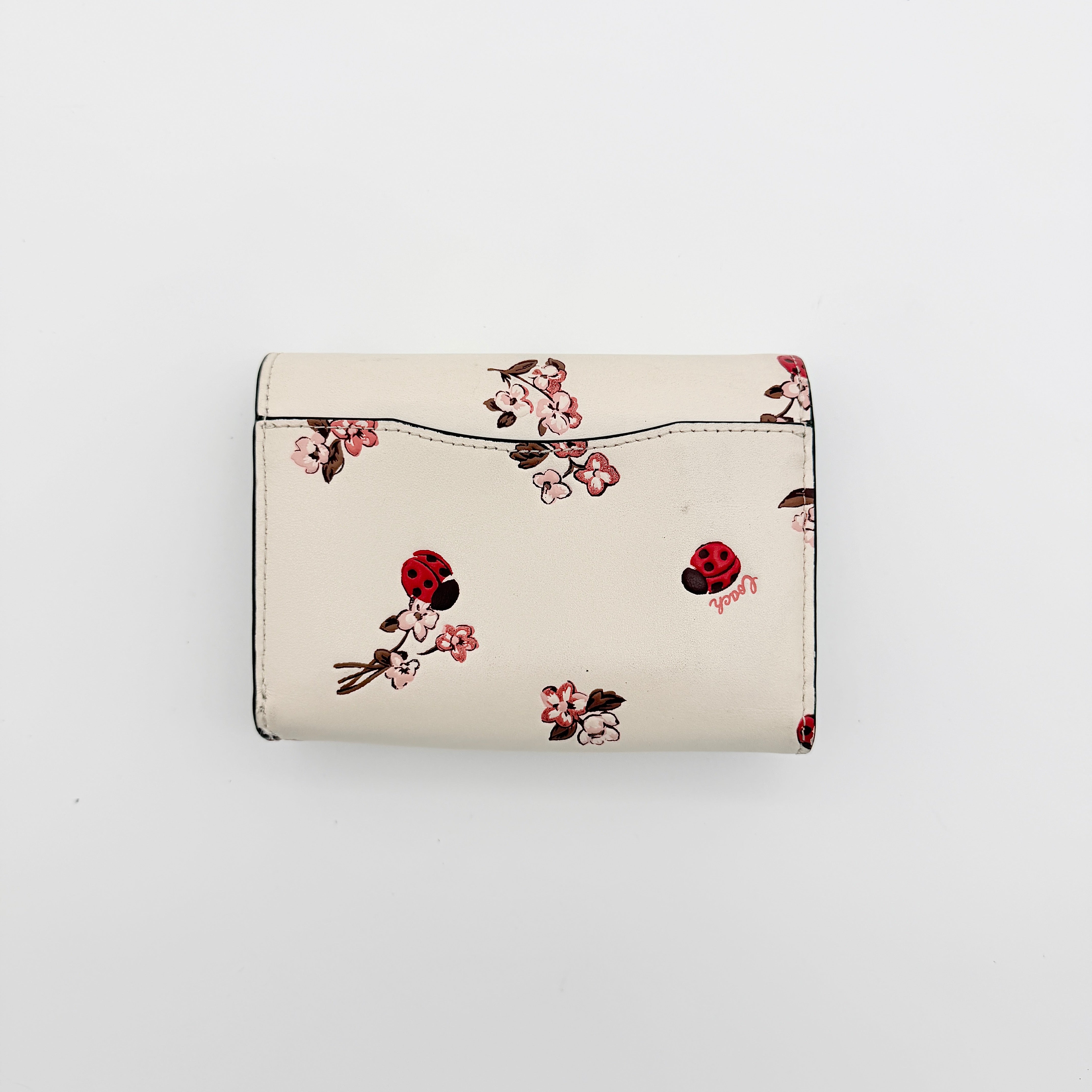 Coach Ladybug Floral Medium Flap Wallet in white leather with playful ladybug and floral print, shown with gold logo on the front.