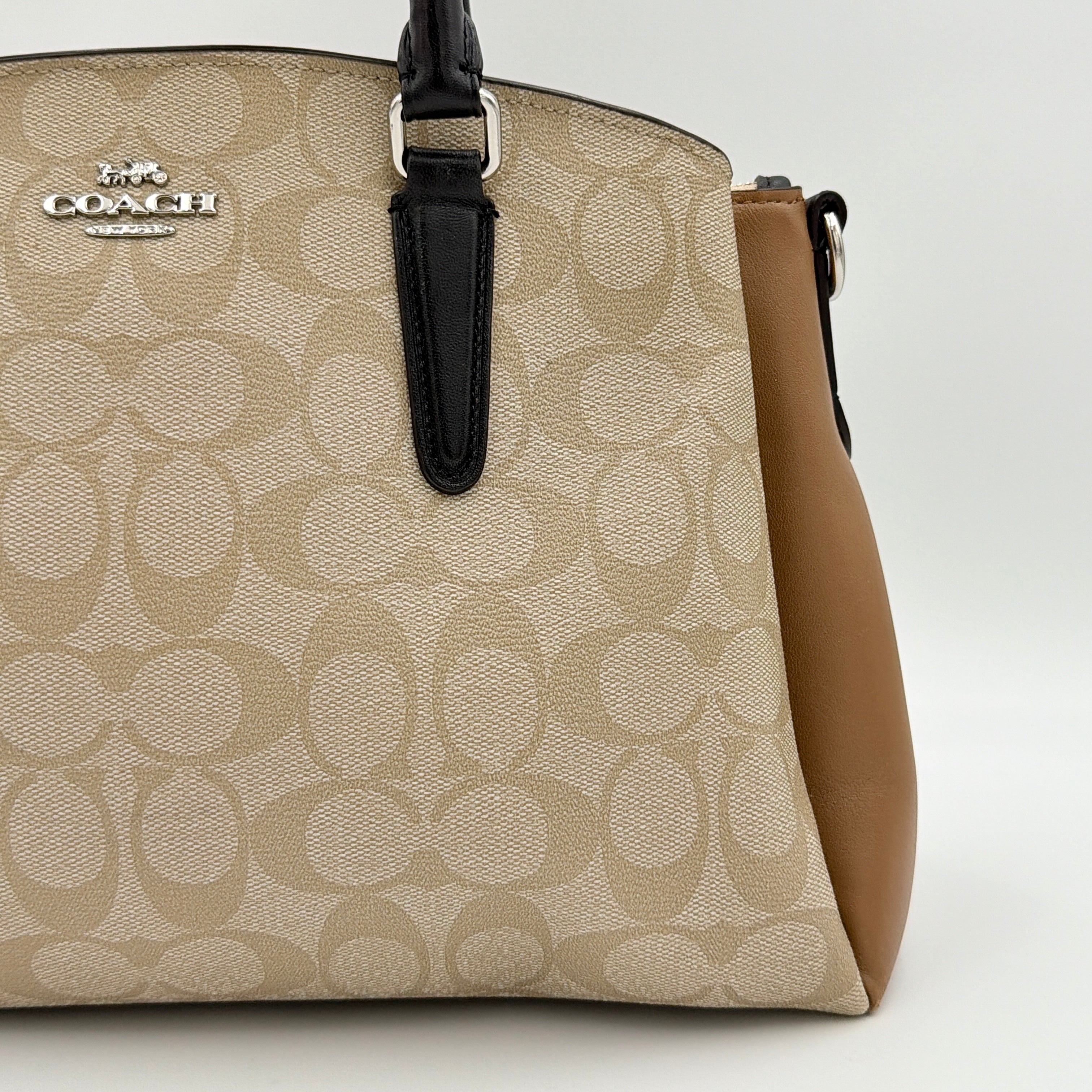 Coach Signature Sage Carryall in beige monogram canvas and tan leather with black handles, styled as an elegant, softly structured handbag.