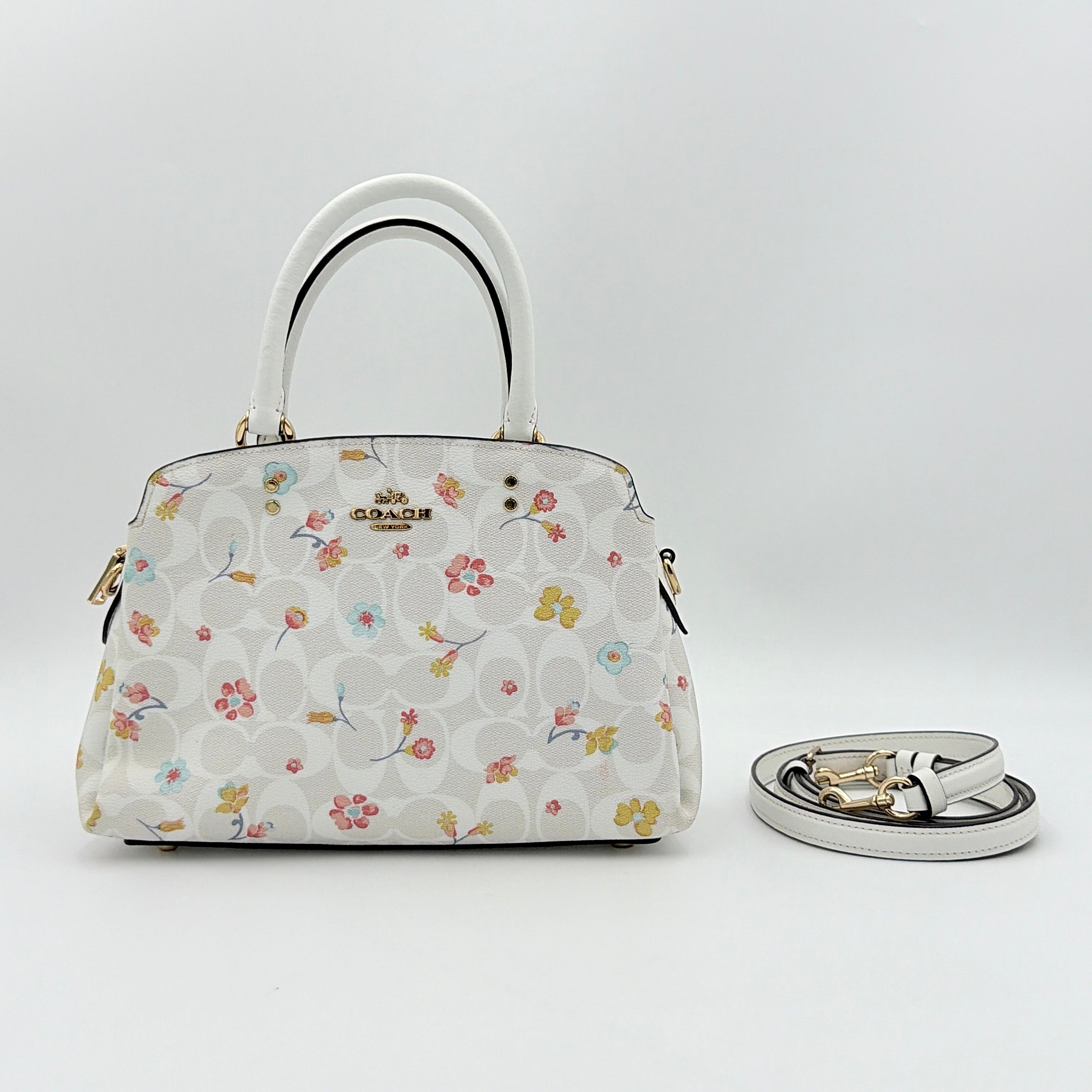 Coach 2Way Signature Lillie Carryall in white canvas with gold hardware and multicolour floral print, accompanied by a detachable white shoulder strap.