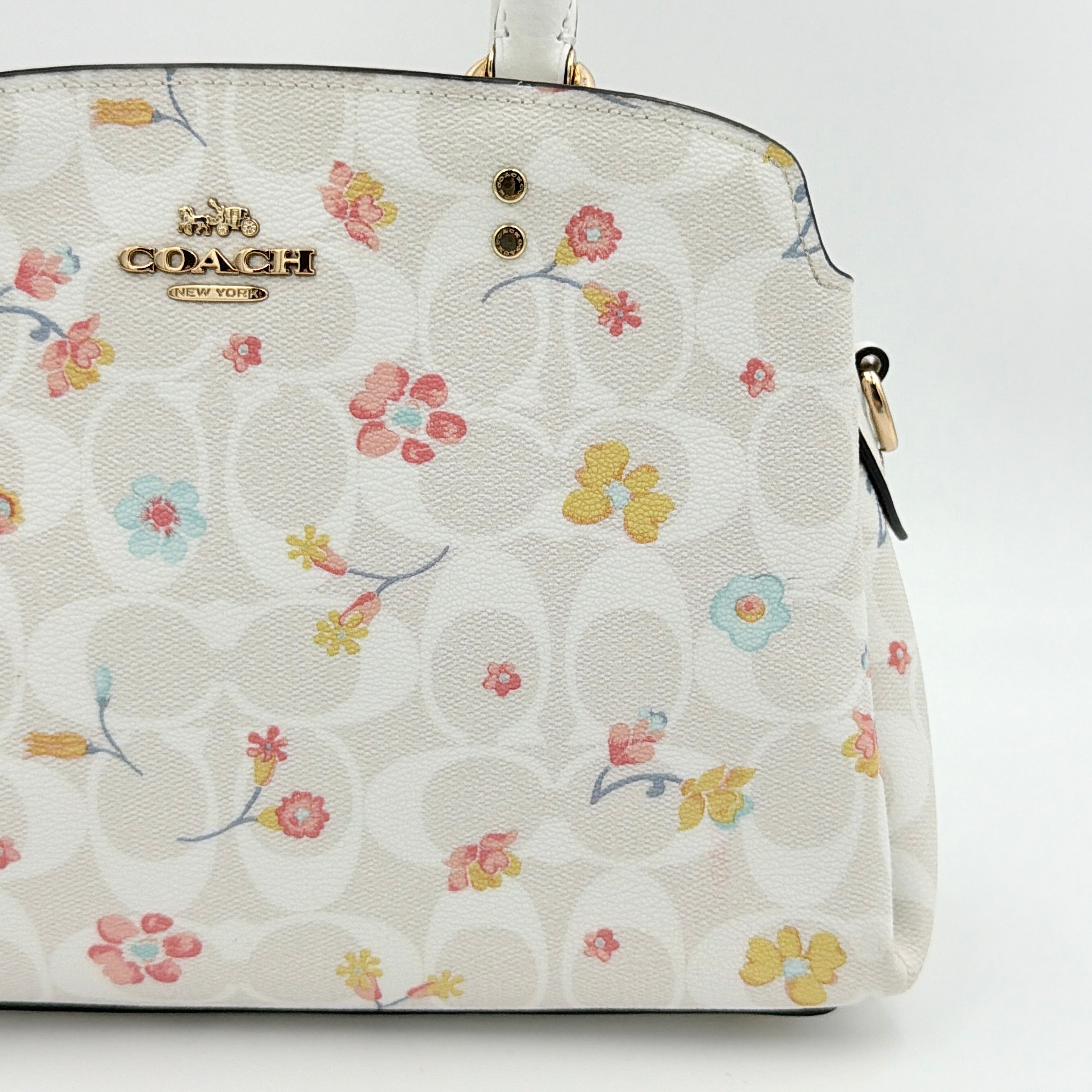 Coach 2Way Signature Lillie Carryall in white canvas with gold hardware and multicolour floral print, accompanied by a detachable white shoulder strap.