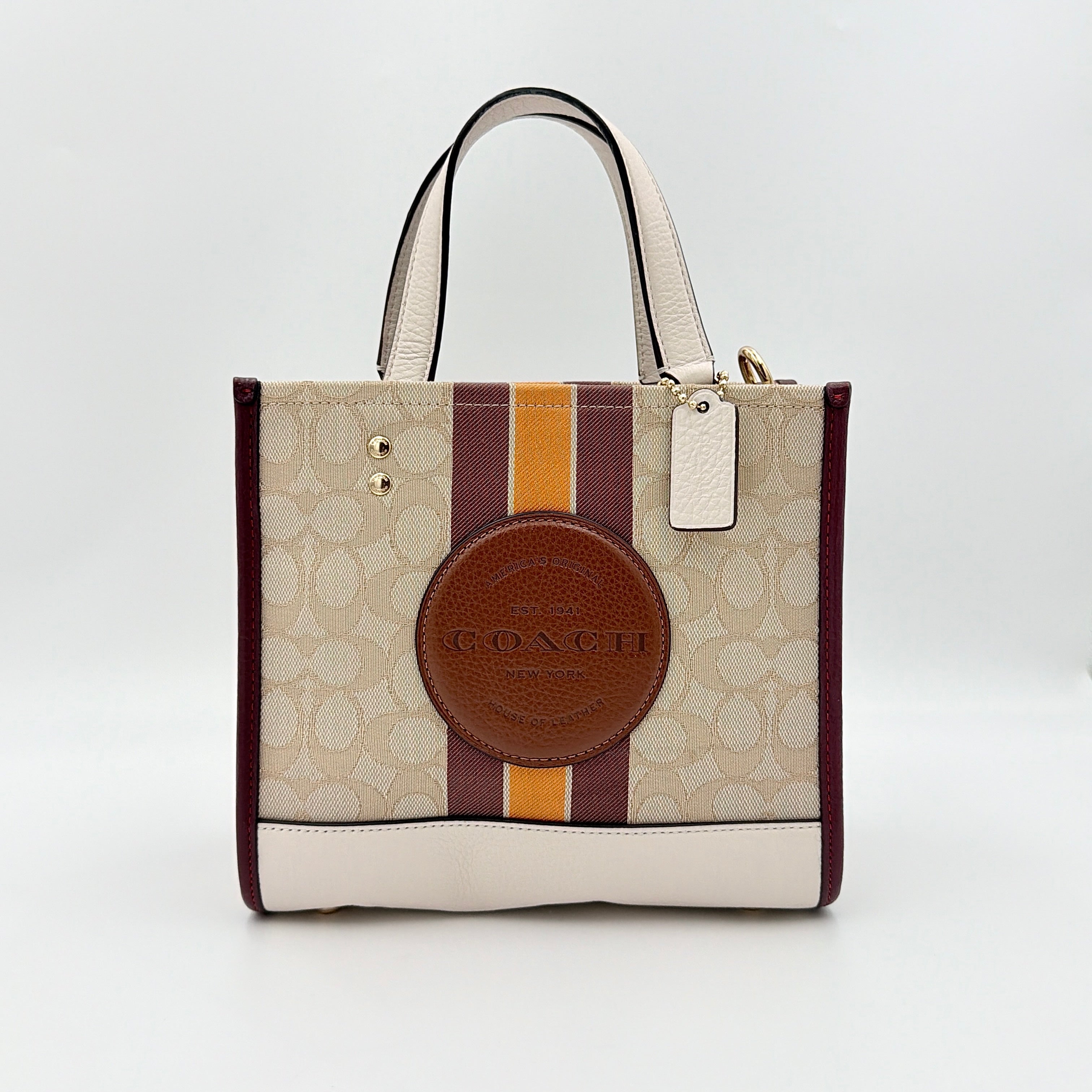 Coach Signature Dempsey 22 Stripe Tote Bag in beige canvas with bold vertical stripes, leather trims, logo patch, and detachable strap.