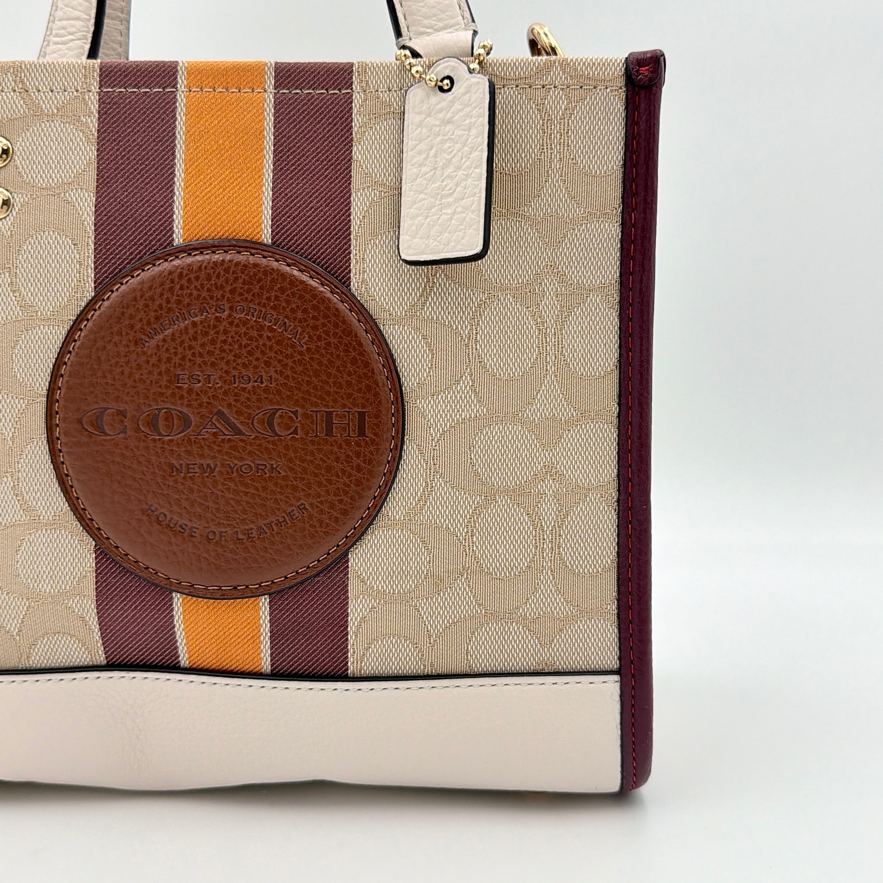 Coach Signature Dempsey 22 Stripe Tote Bag in beige canvas with bold vertical stripes, leather trims, logo patch, and detachable strap.