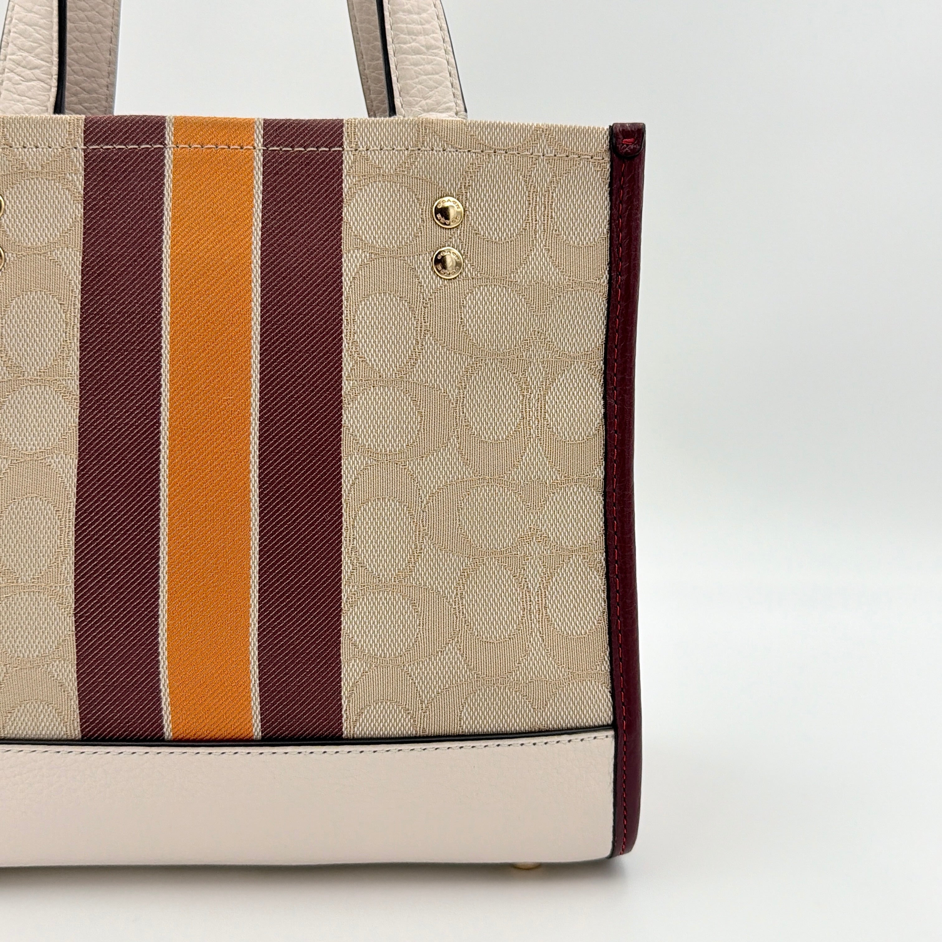 Coach Signature Dempsey 22 Stripe Tote Bag in beige canvas with bold vertical stripes, leather trims, logo patch, and detachable strap.