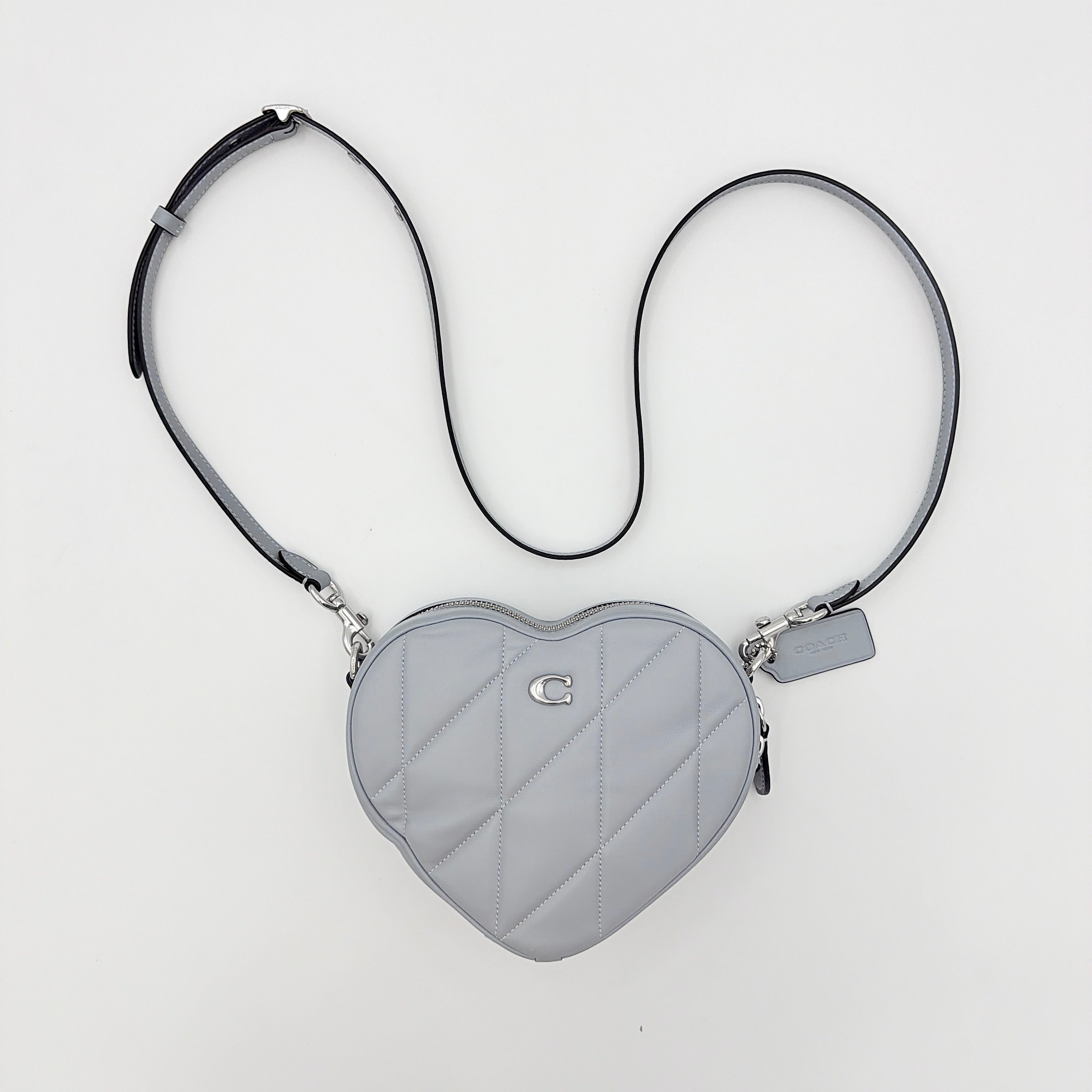 Coach heart-shaped quilted grey crossbody bag with silver hardware and adjustable strap.