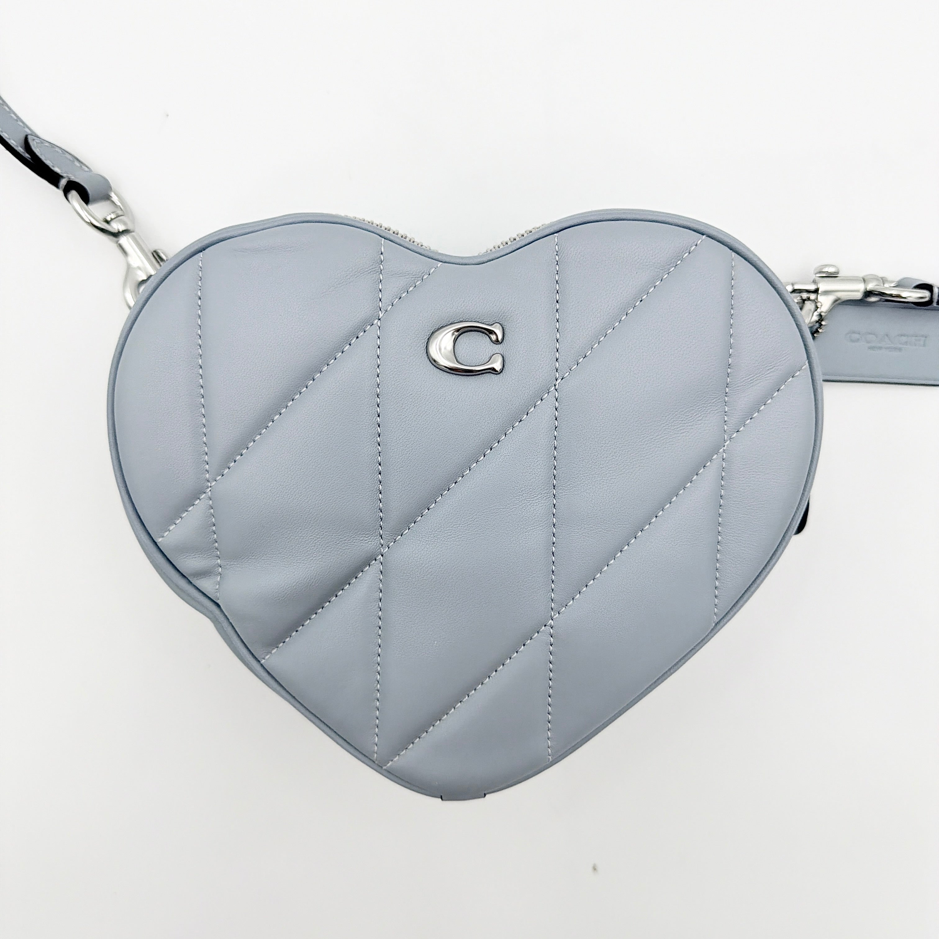 Coach heart-shaped quilted grey crossbody bag with silver hardware and adjustable strap.