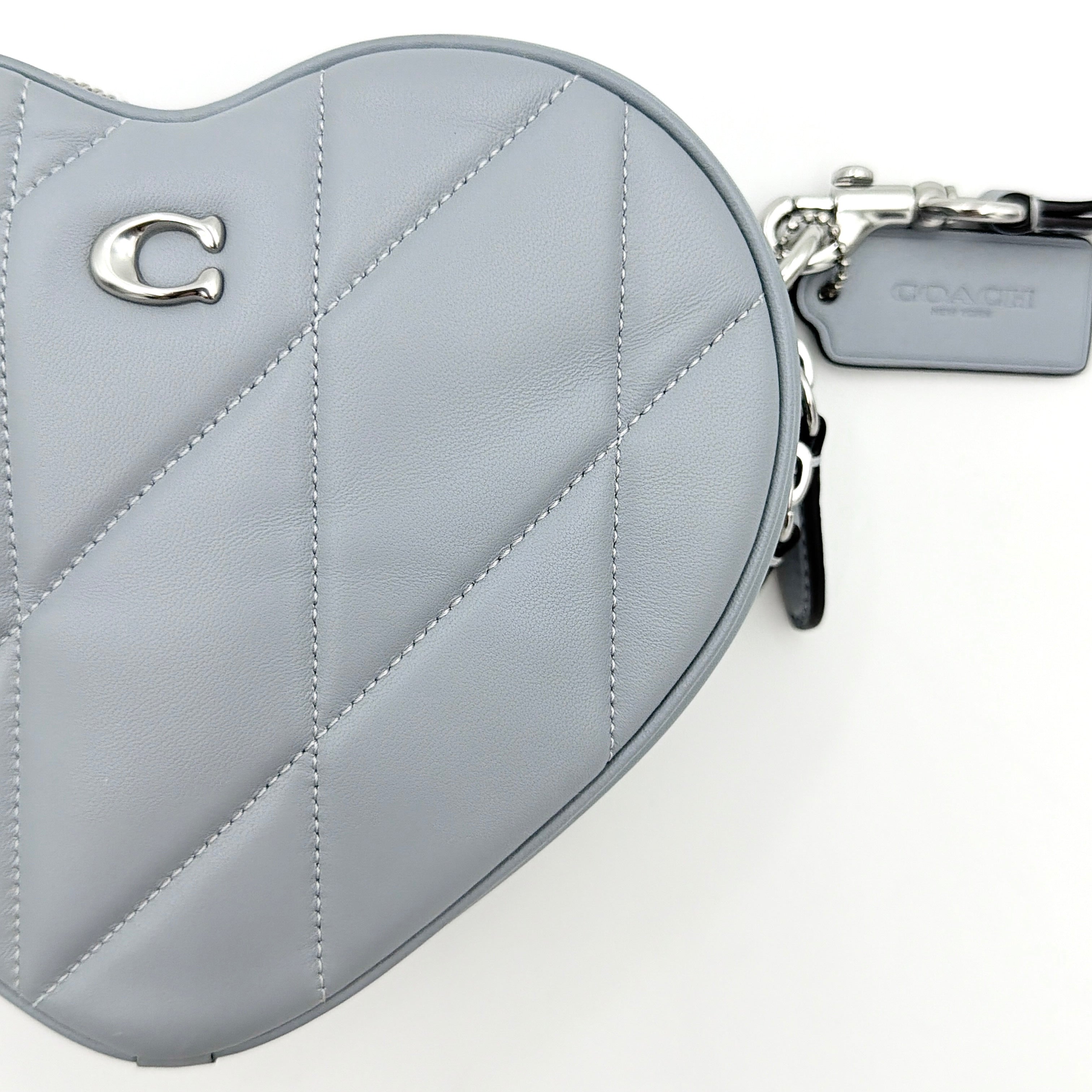 Coach heart-shaped quilted grey crossbody bag with silver hardware and adjustable strap.