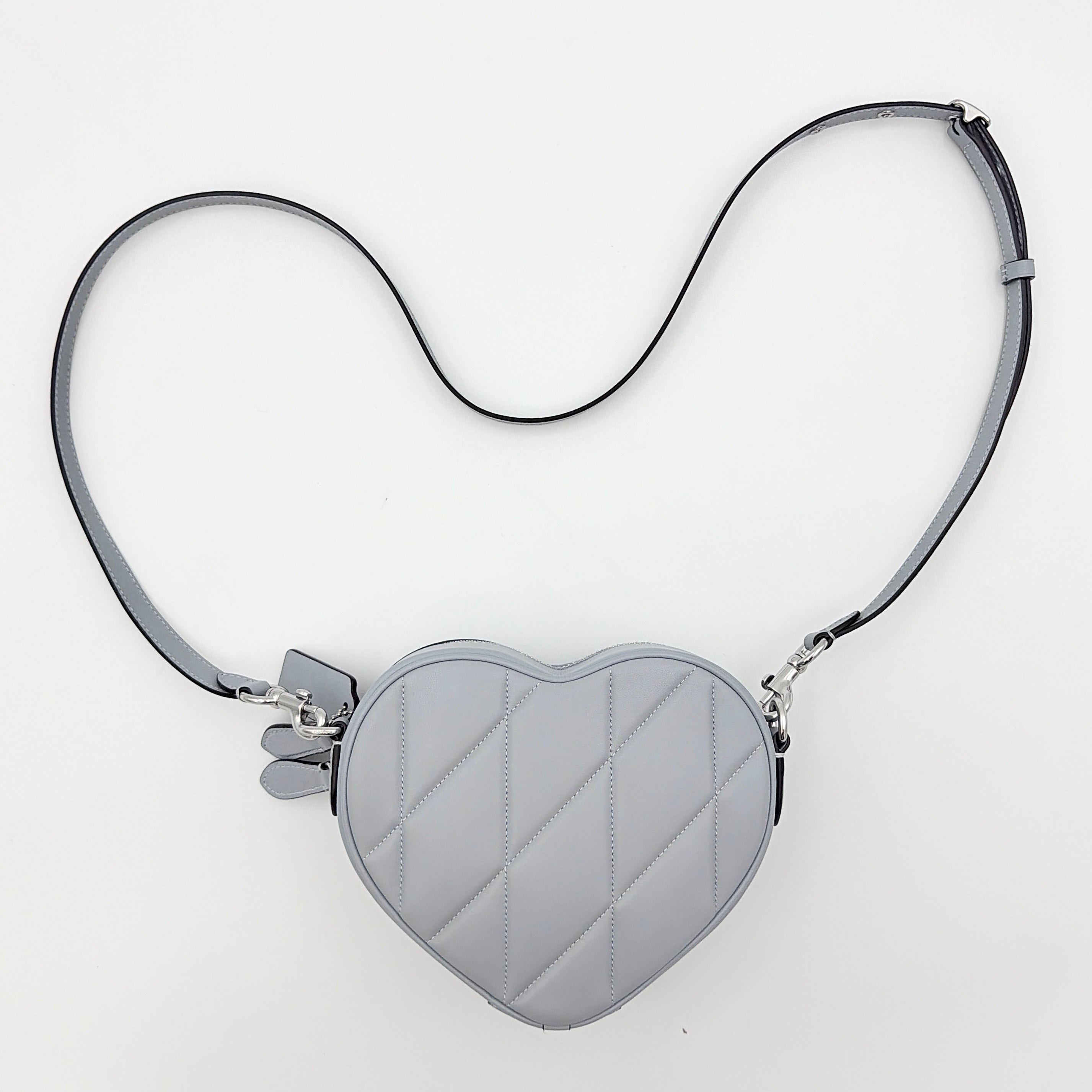 Coach heart-shaped quilted grey crossbody bag with silver hardware and adjustable strap.