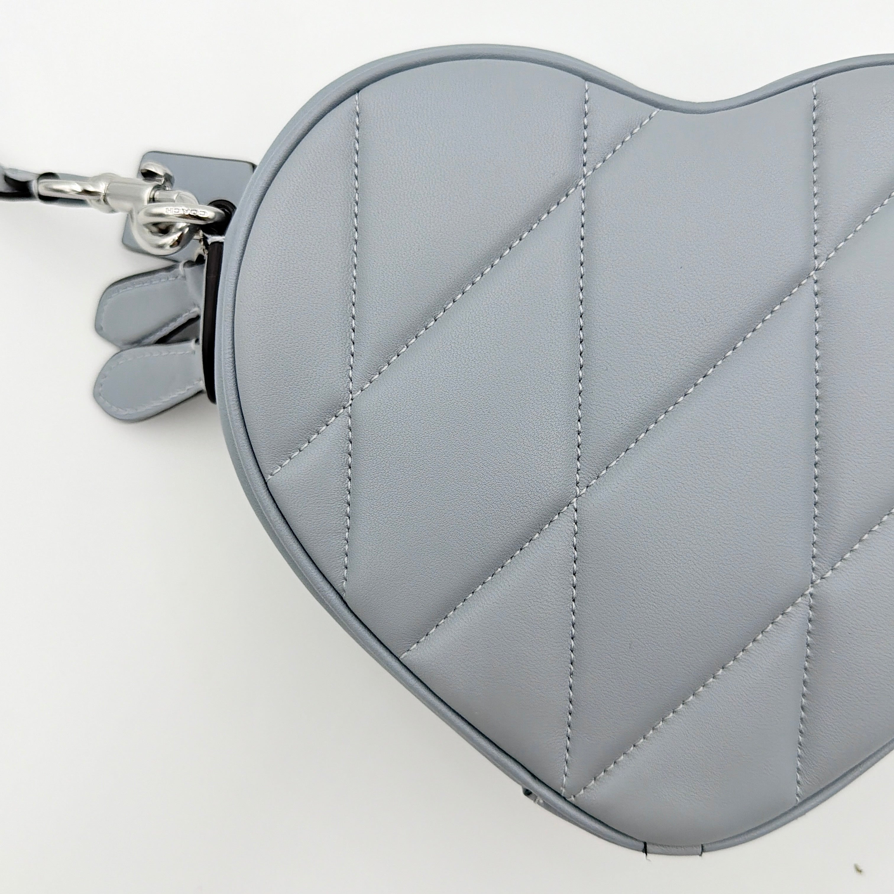 Coach heart-shaped quilted grey crossbody bag with silver hardware and adjustable strap.