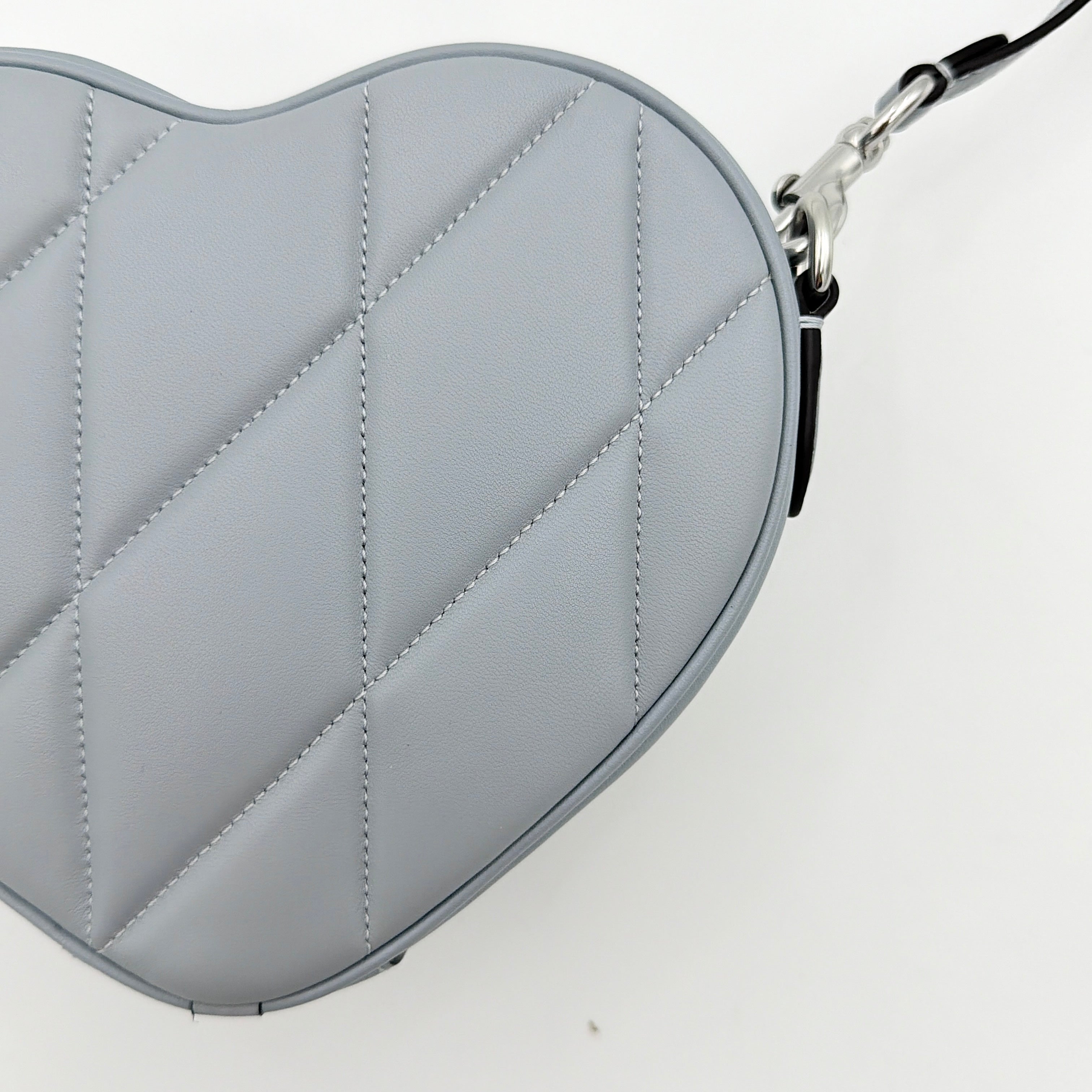 Coach heart-shaped quilted grey crossbody bag with silver hardware and adjustable strap.