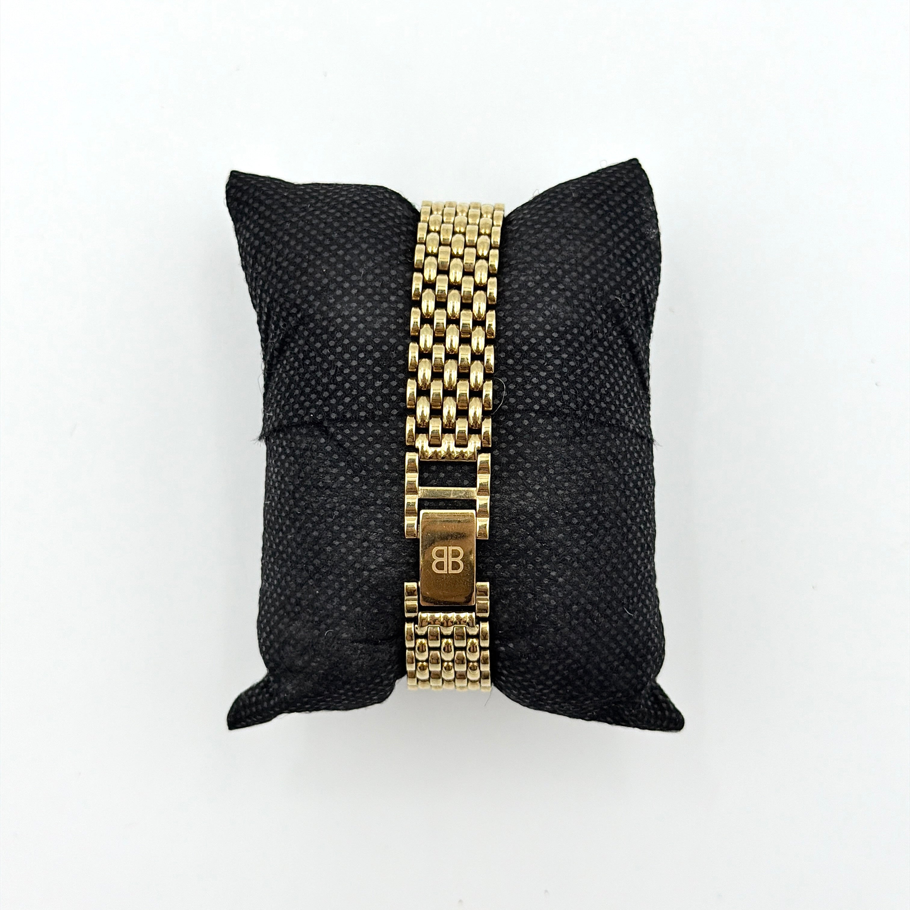 Balenciaga BB Quartz gold watch with a round dial, diamond-shaped hour markers, and a gold link bracelet displayed on a black cushion.