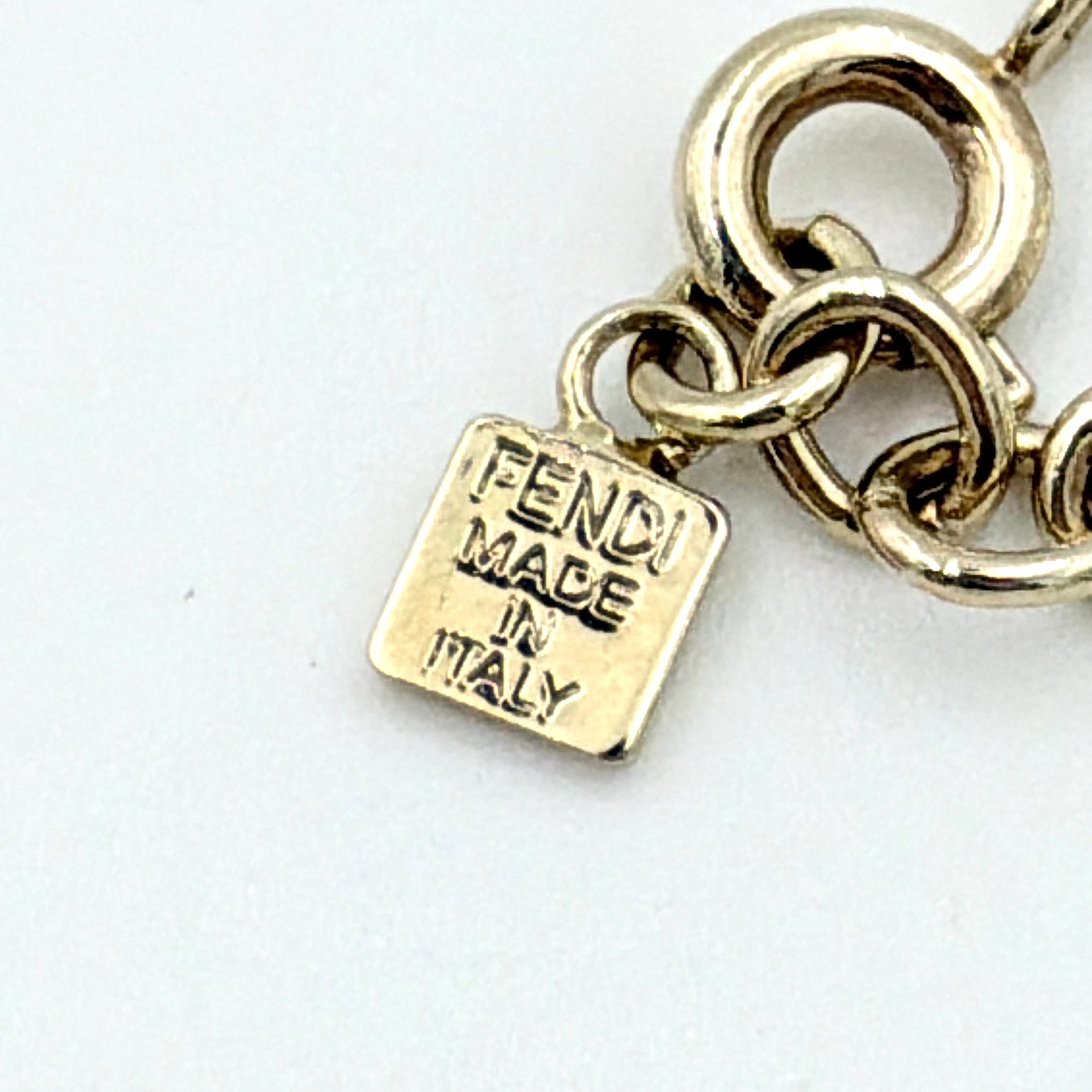 A gold-tone Fendi bracelet with a flowing logo script and adjustable chain, styled with a branded charm.