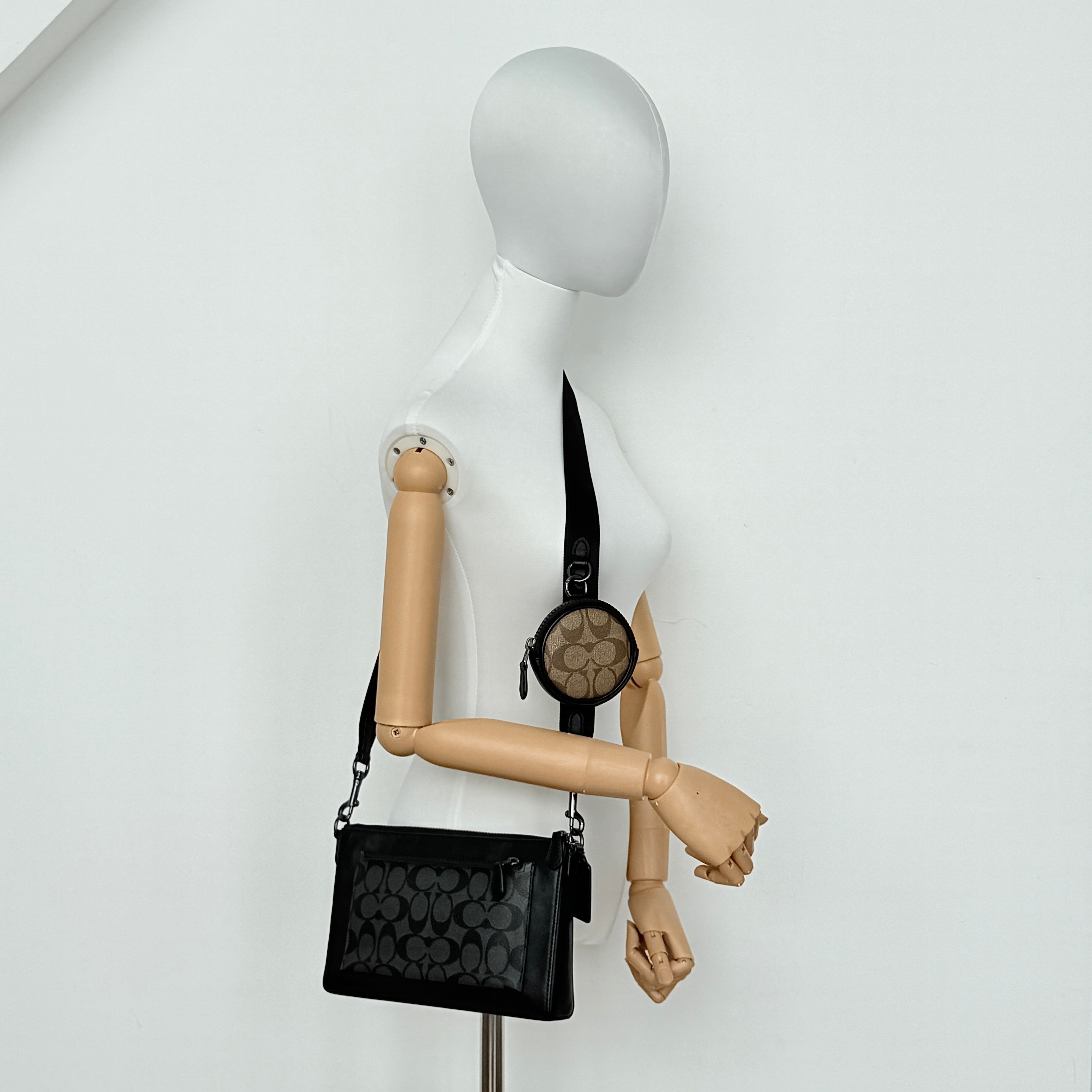 Coach Signature Holden Crossbody Bag in black with beige round coin pouch, featuring coated canvas and leather panels against a white background.