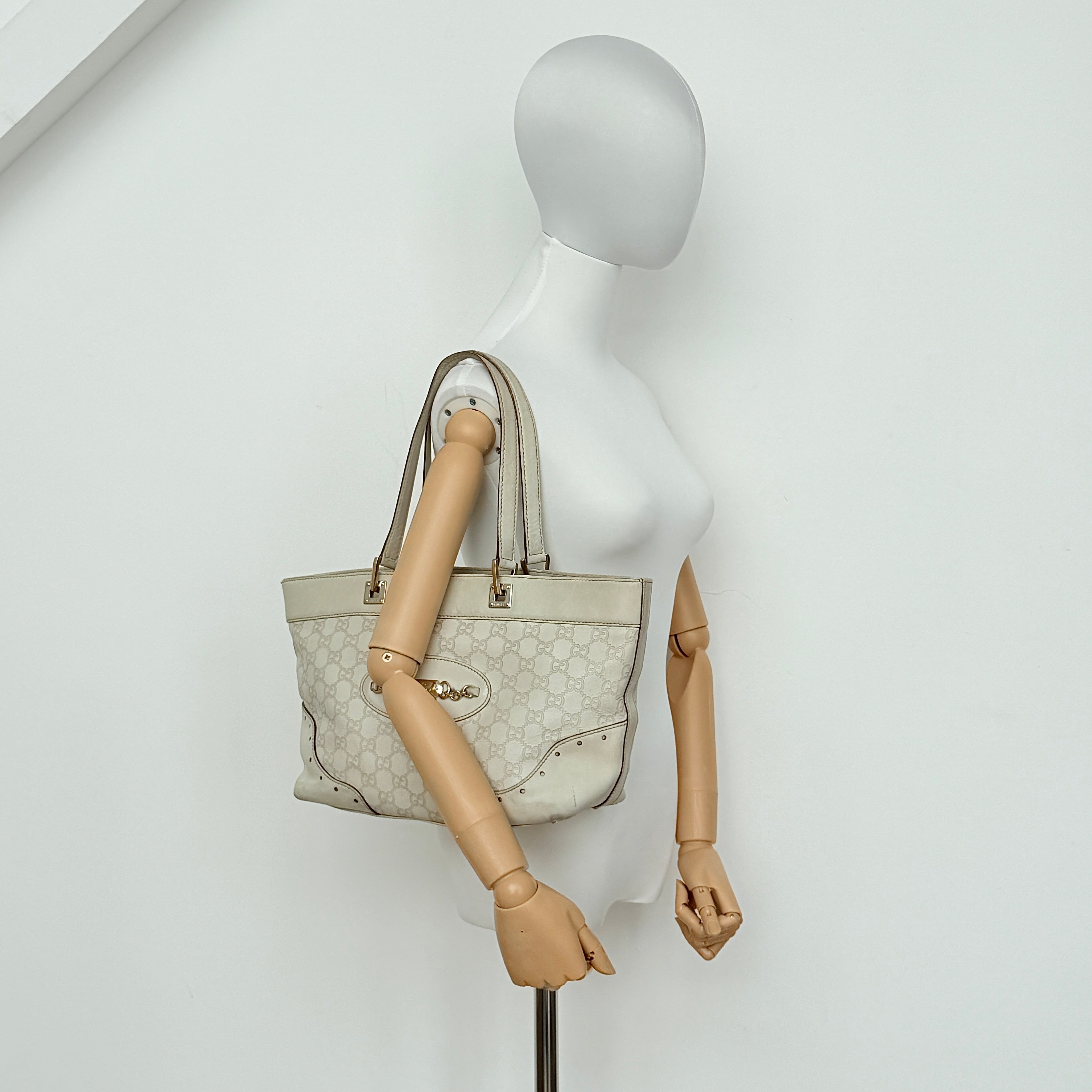 Cream Gucci GG Monogram Guccissima Punch Shoulder Bag with gold hardware, sculpted corners, and double top handles against a white background.