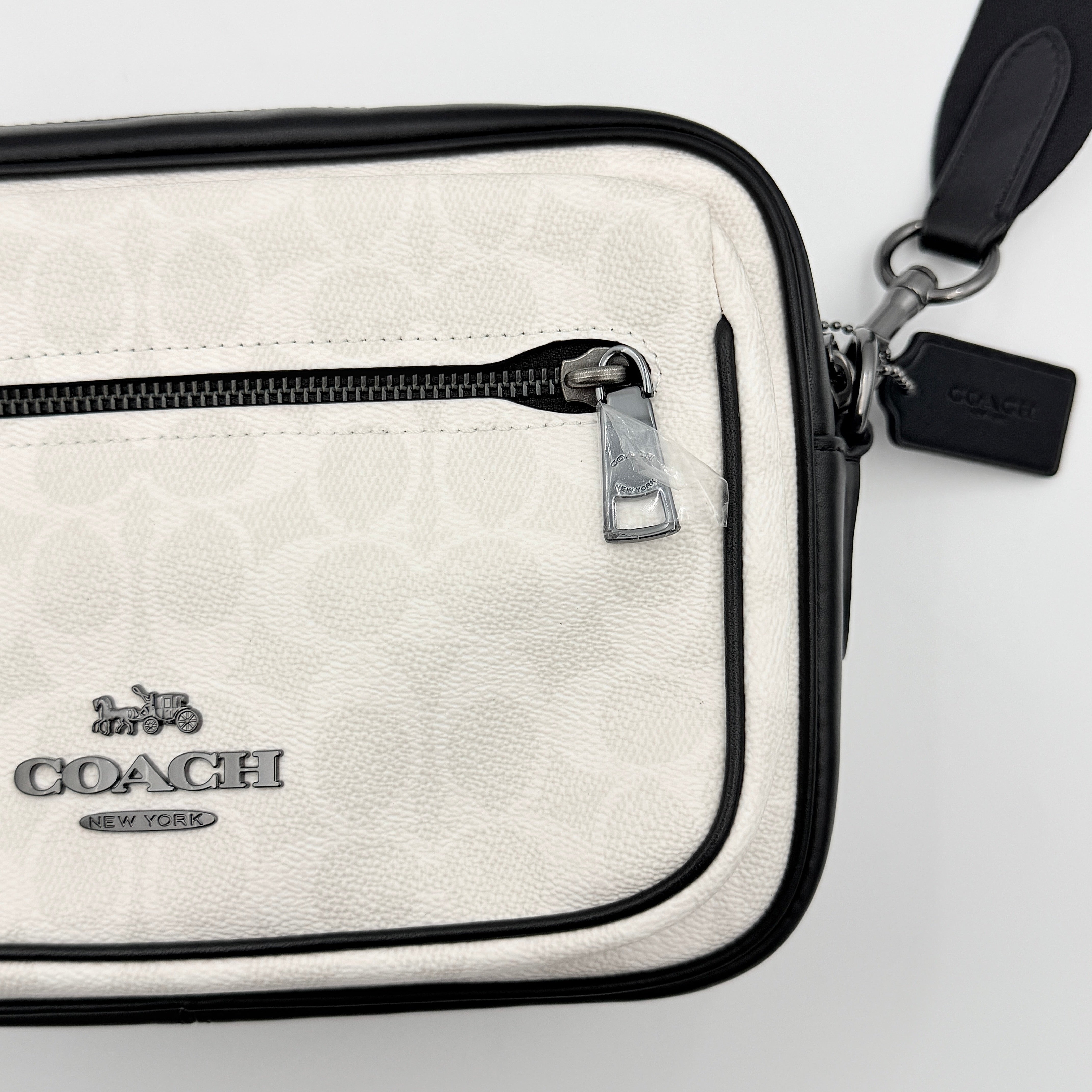 Coach Signature Elias Crossbody Bag in white canvas with black leather trim and silver hardware, styled with an adjustable black strap.