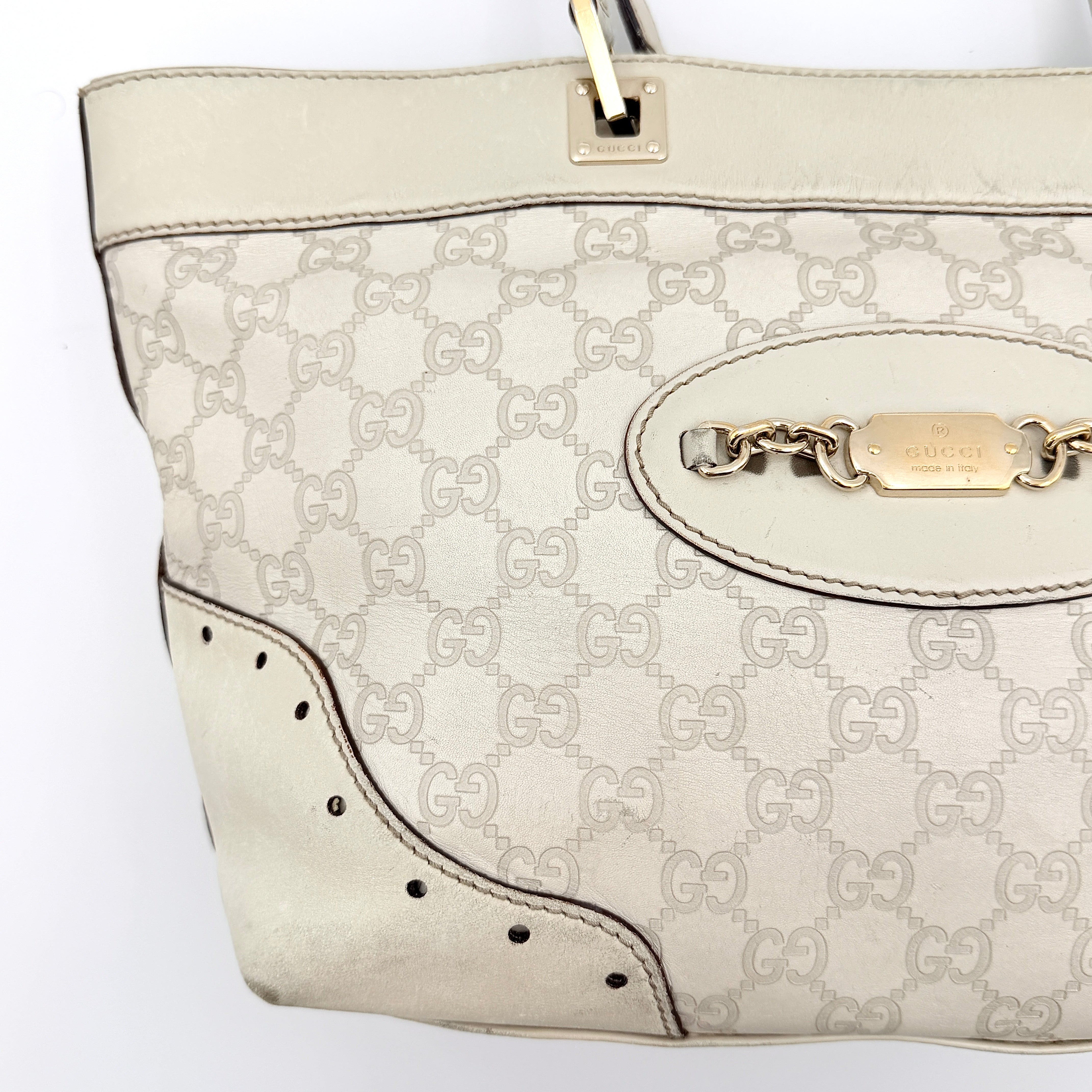 Cream Gucci GG Monogram Guccissima Punch Shoulder Bag with gold hardware, sculpted corners, and double top handles against a white background.