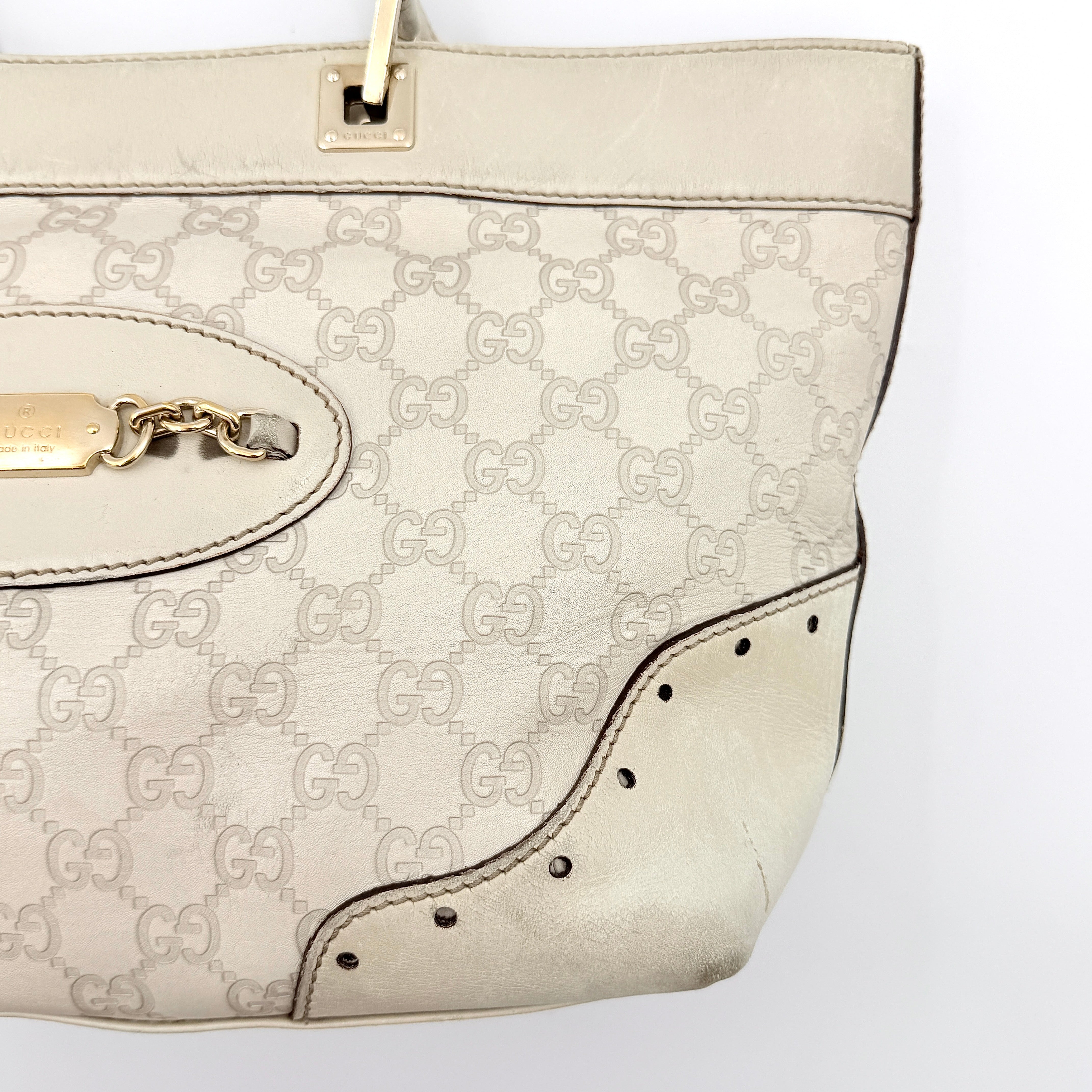 Cream Gucci GG Monogram Guccissima Punch Shoulder Bag with gold hardware, sculpted corners, and double top handles against a white background.
