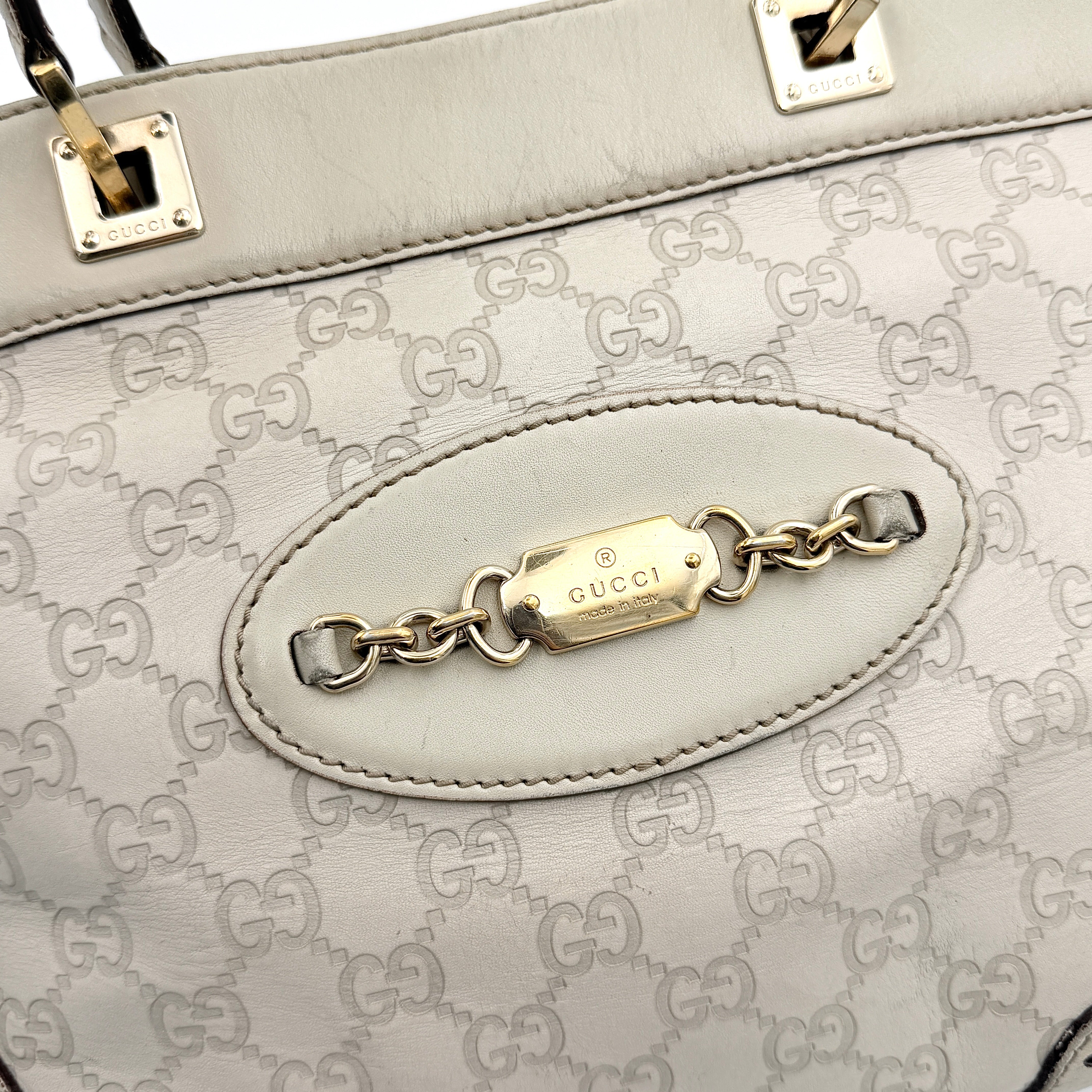 Cream Gucci GG Monogram Guccissima Punch Shoulder Bag with gold hardware, sculpted corners, and double top handles against a white background.