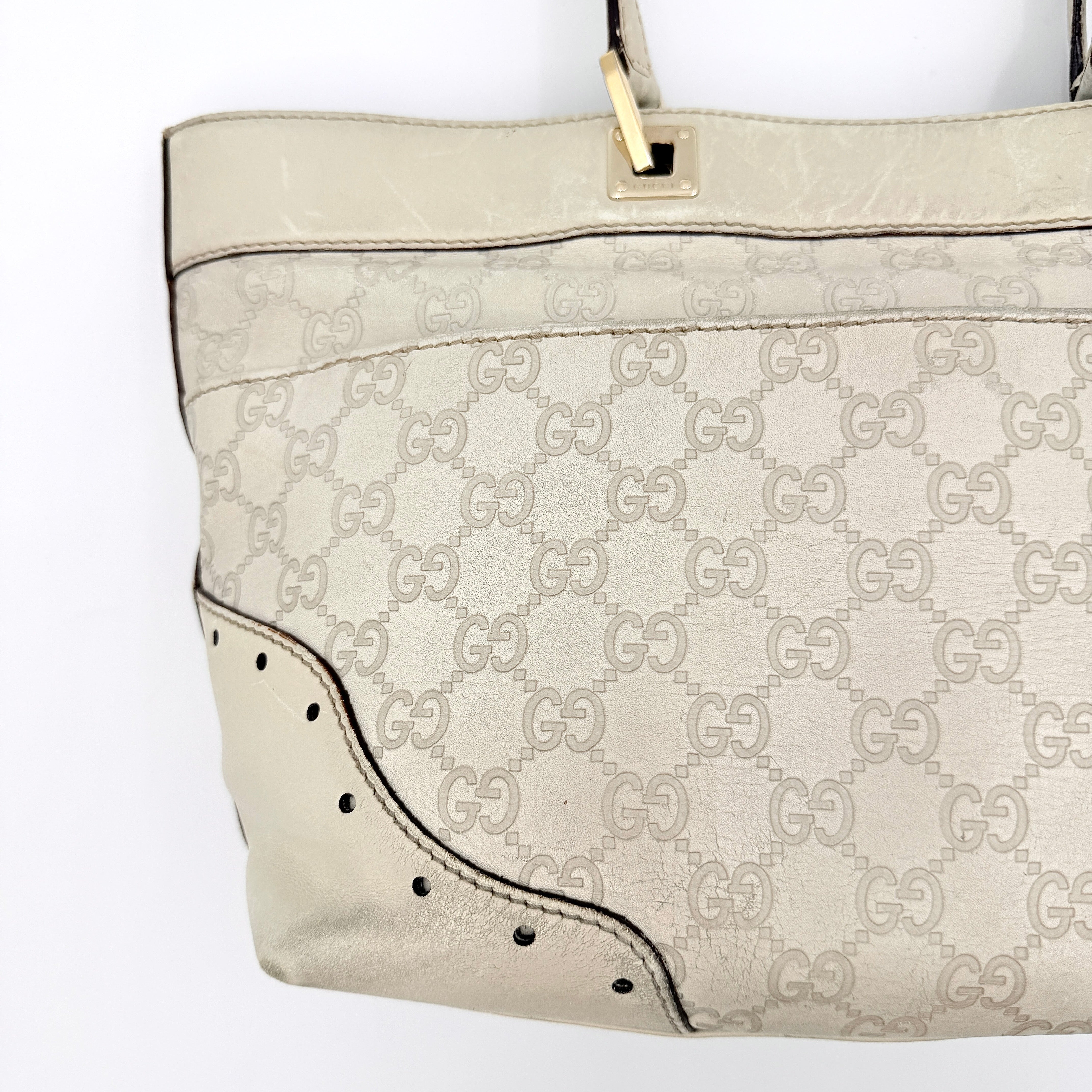 Cream Gucci GG Monogram Guccissima Punch Shoulder Bag with gold hardware, sculpted corners, and double top handles against a white background.