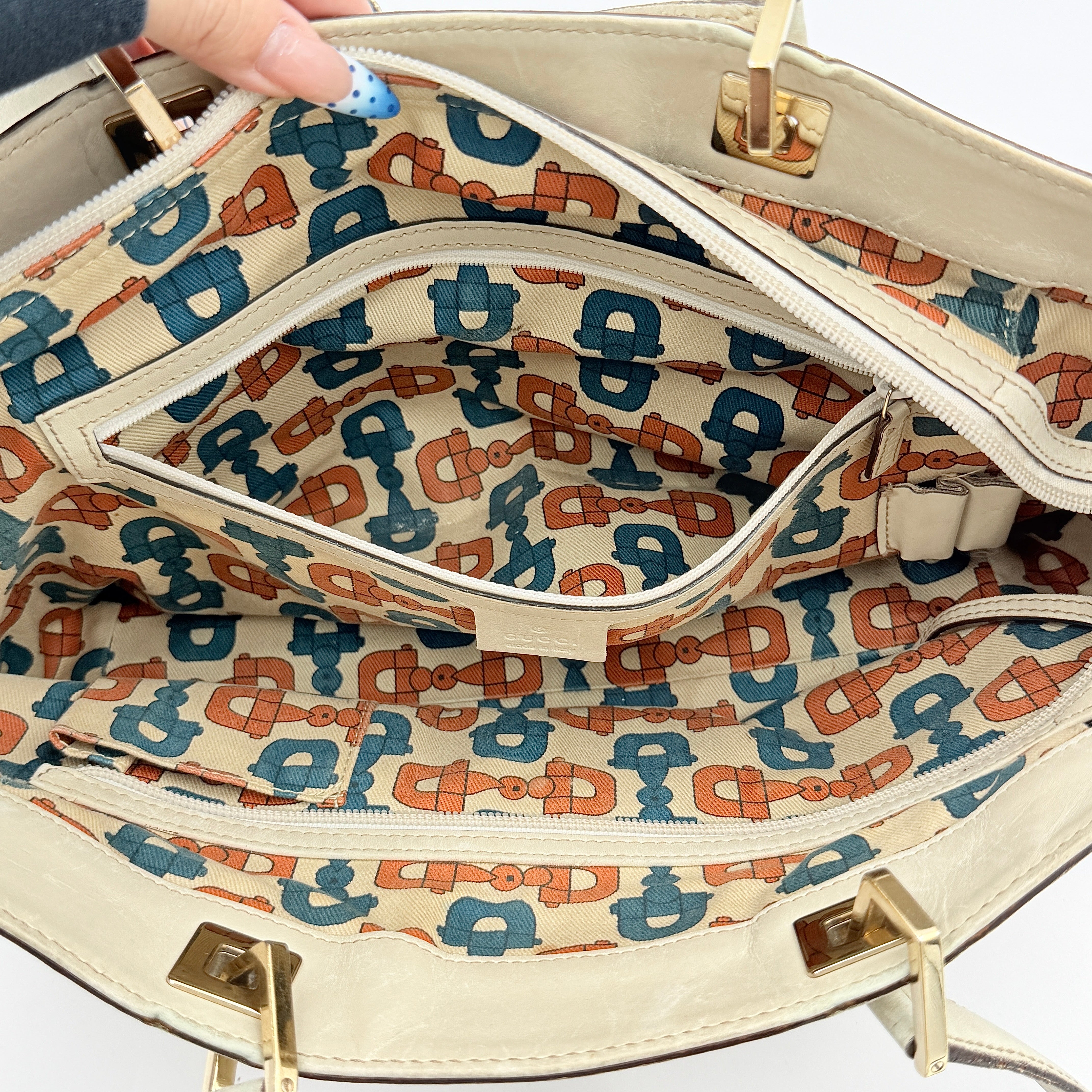 Cream Gucci GG Monogram Guccissima Punch Shoulder Bag with gold hardware, sculpted corners, and double top handles against a white background.