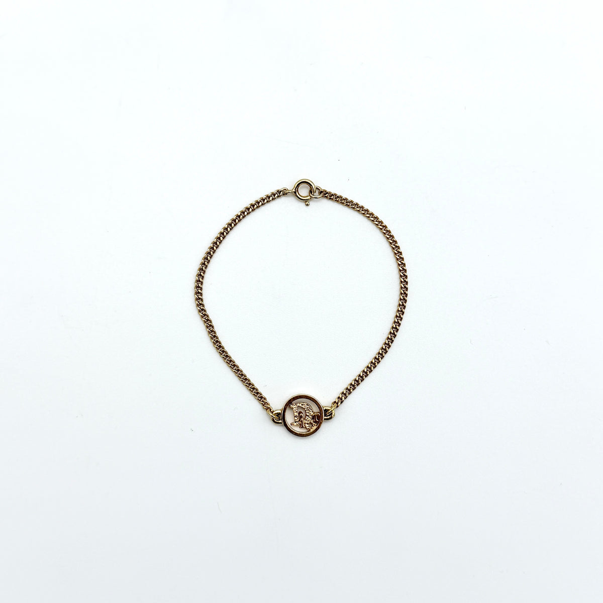 Dior gold-tone logo circle bracelet featuring a curb chain and textured central Dior emblem, photographed on a white background.