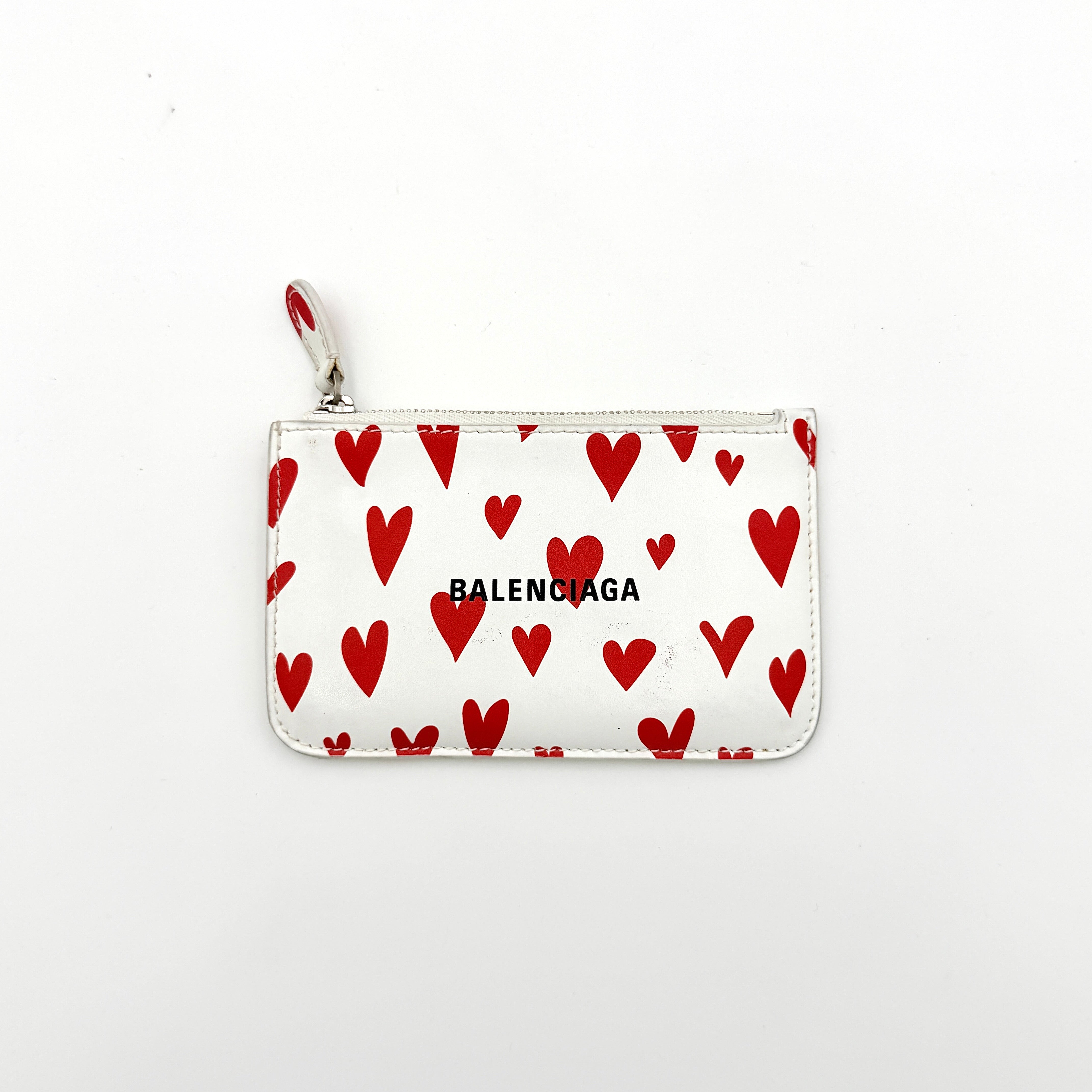 Balenciaga white leather card holder with playful red hearts and zip closure, set against a clean background.