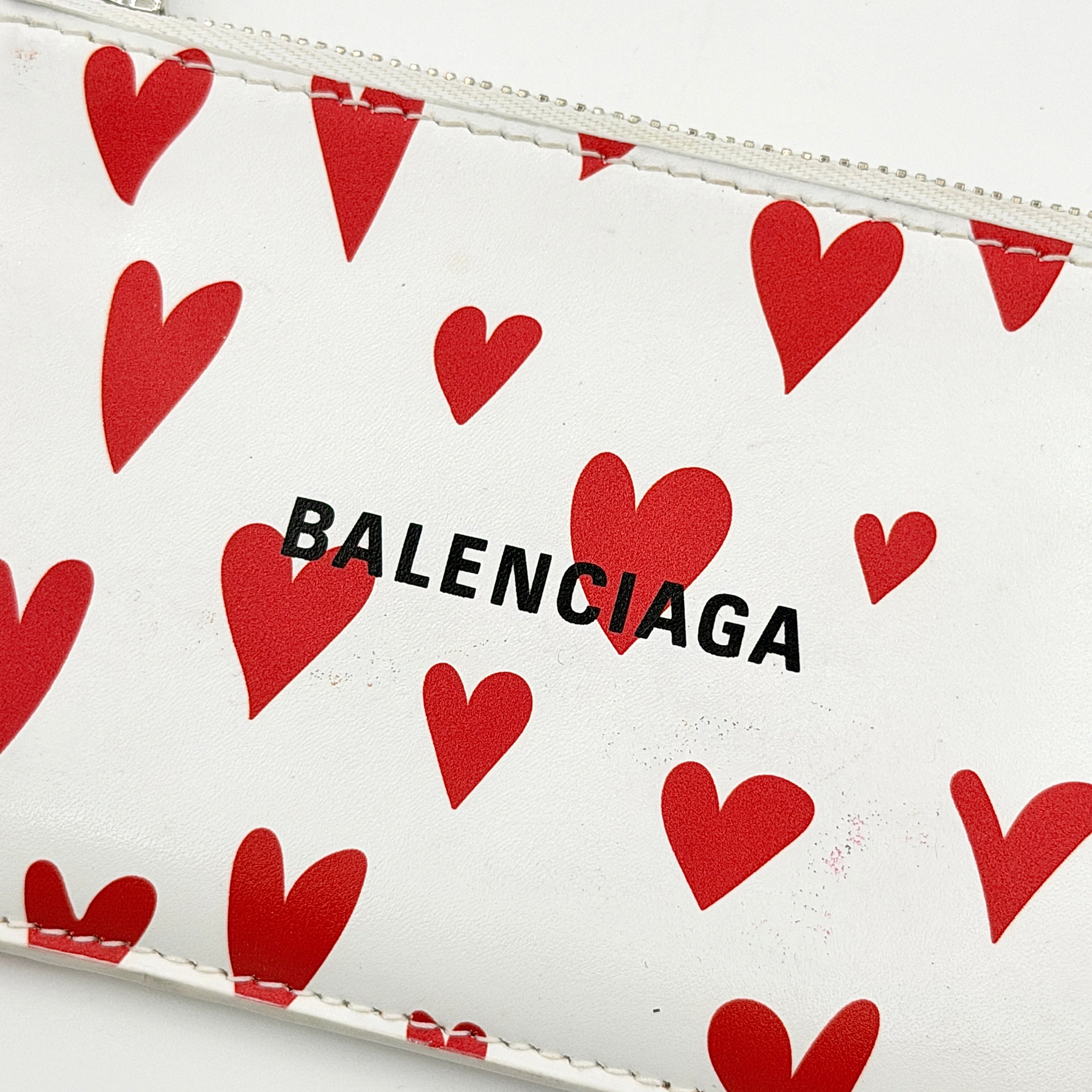 Balenciaga white leather card holder with playful red hearts and zip closure, set against a clean background.