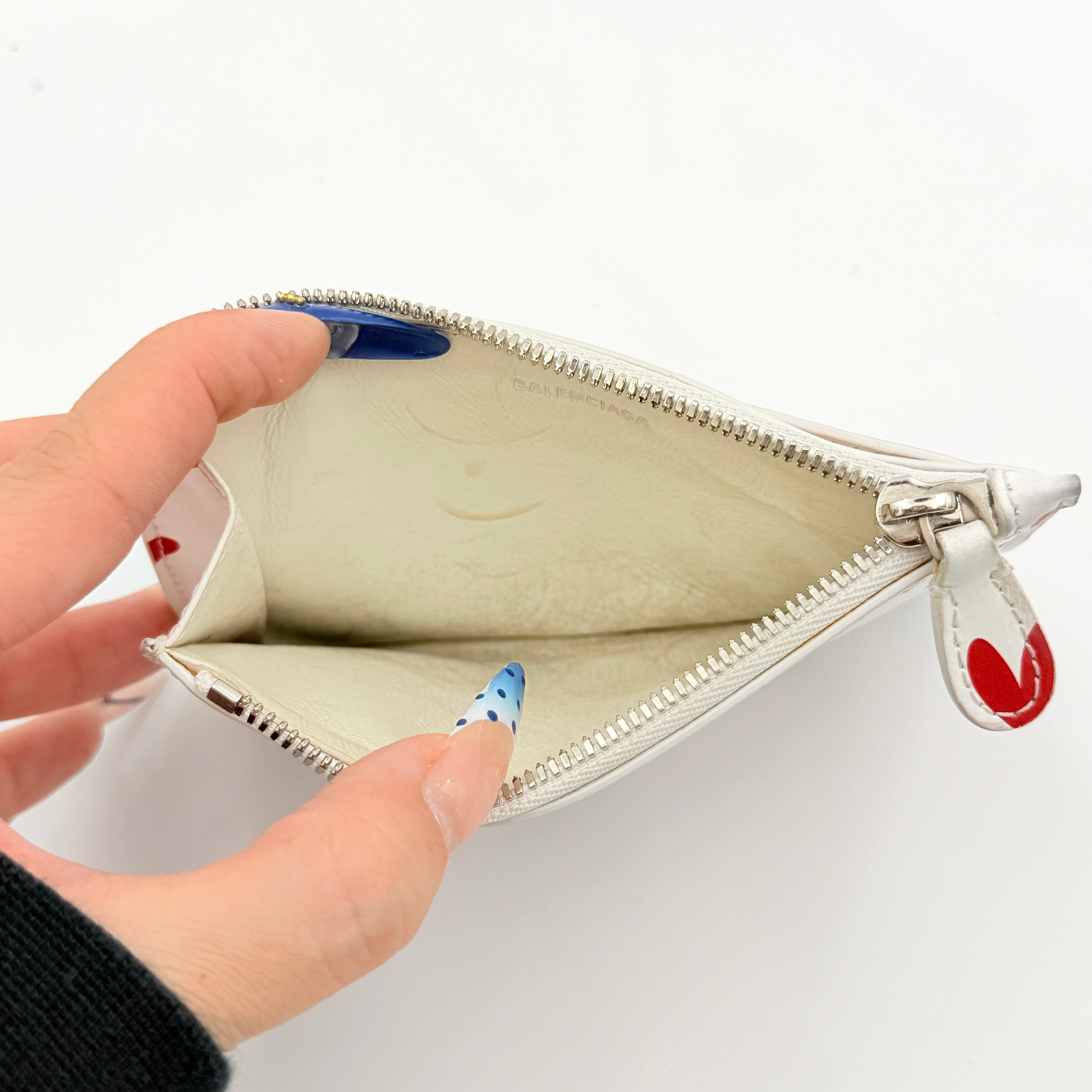 Balenciaga white leather card holder with playful red hearts and zip closure, set against a clean background.