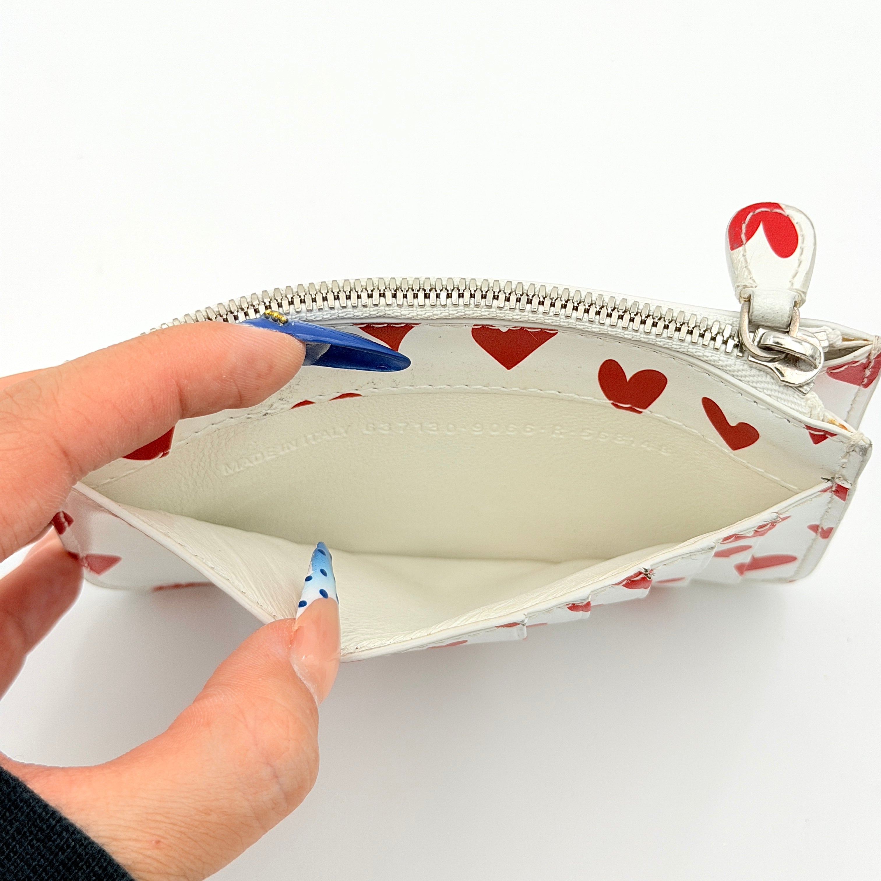 Balenciaga white leather card holder with playful red hearts and zip closure, set against a clean background.