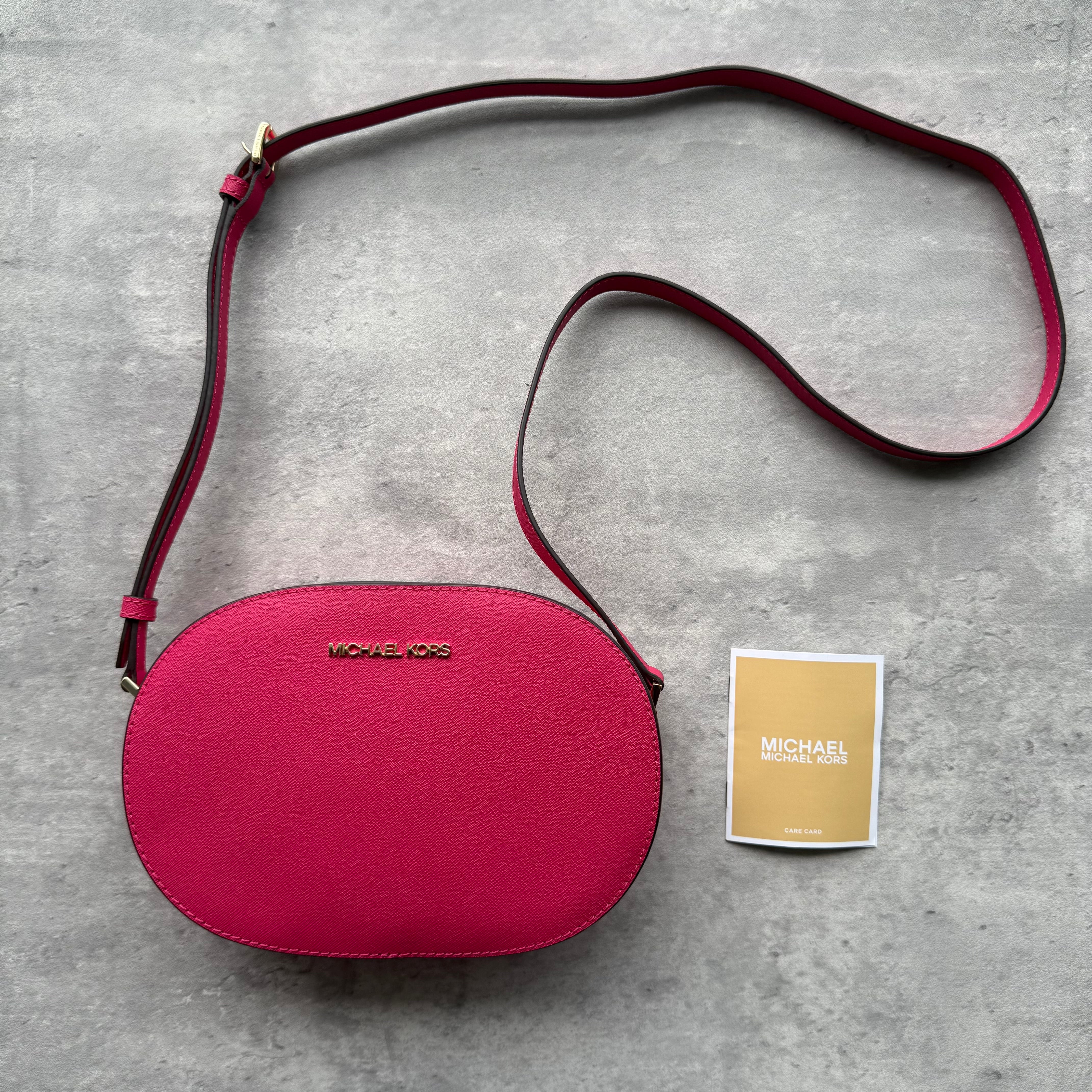 Michael Kors Jet Set Travel Saffiano Leather Crossbody Bag in pink with gold-tone logo, oval silhouette, adjustable strap, and zip-around closure.