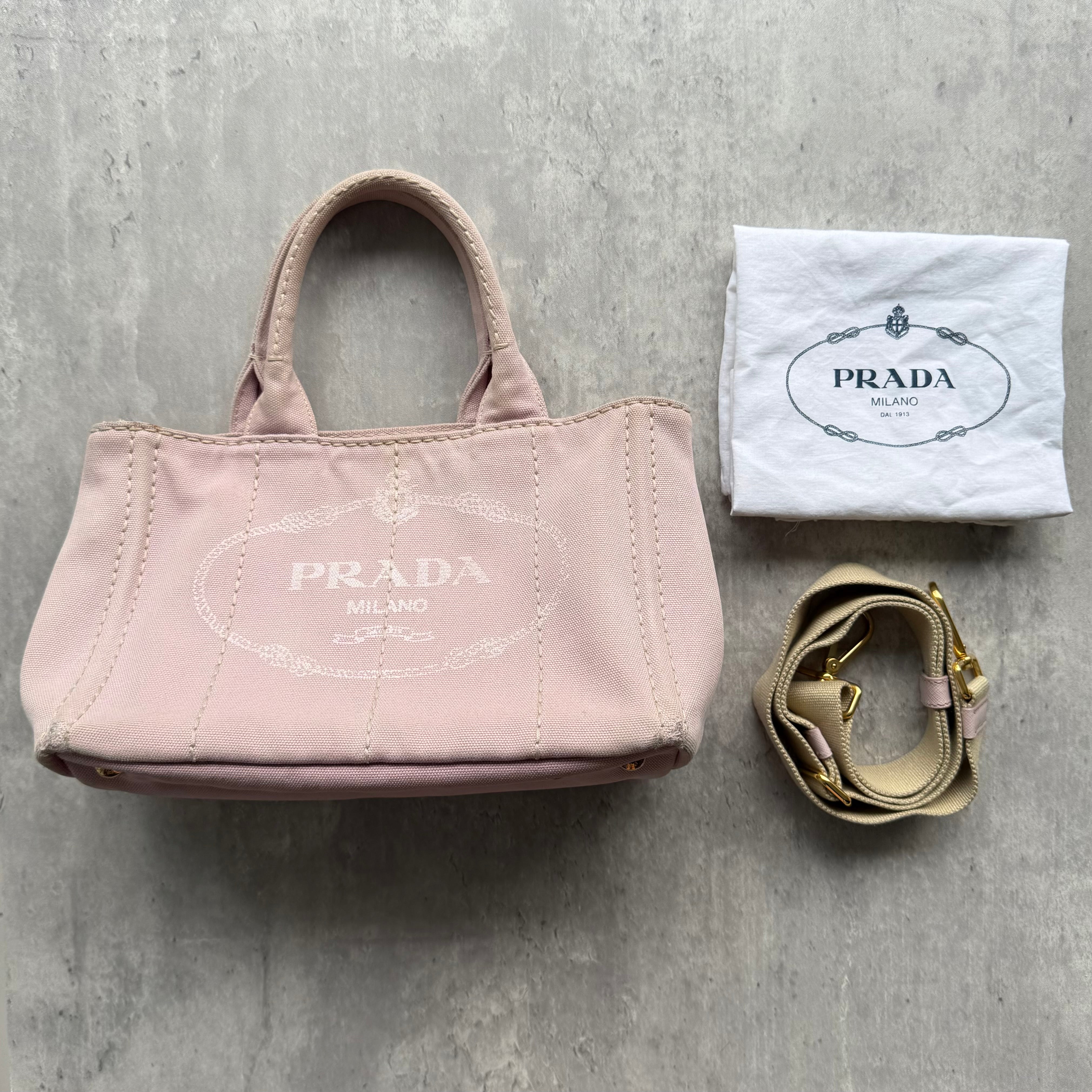 Prada Canapa Tote Bag in light pink canvas with white printed logo, gold-tone hardware, and detachable shoulder strap