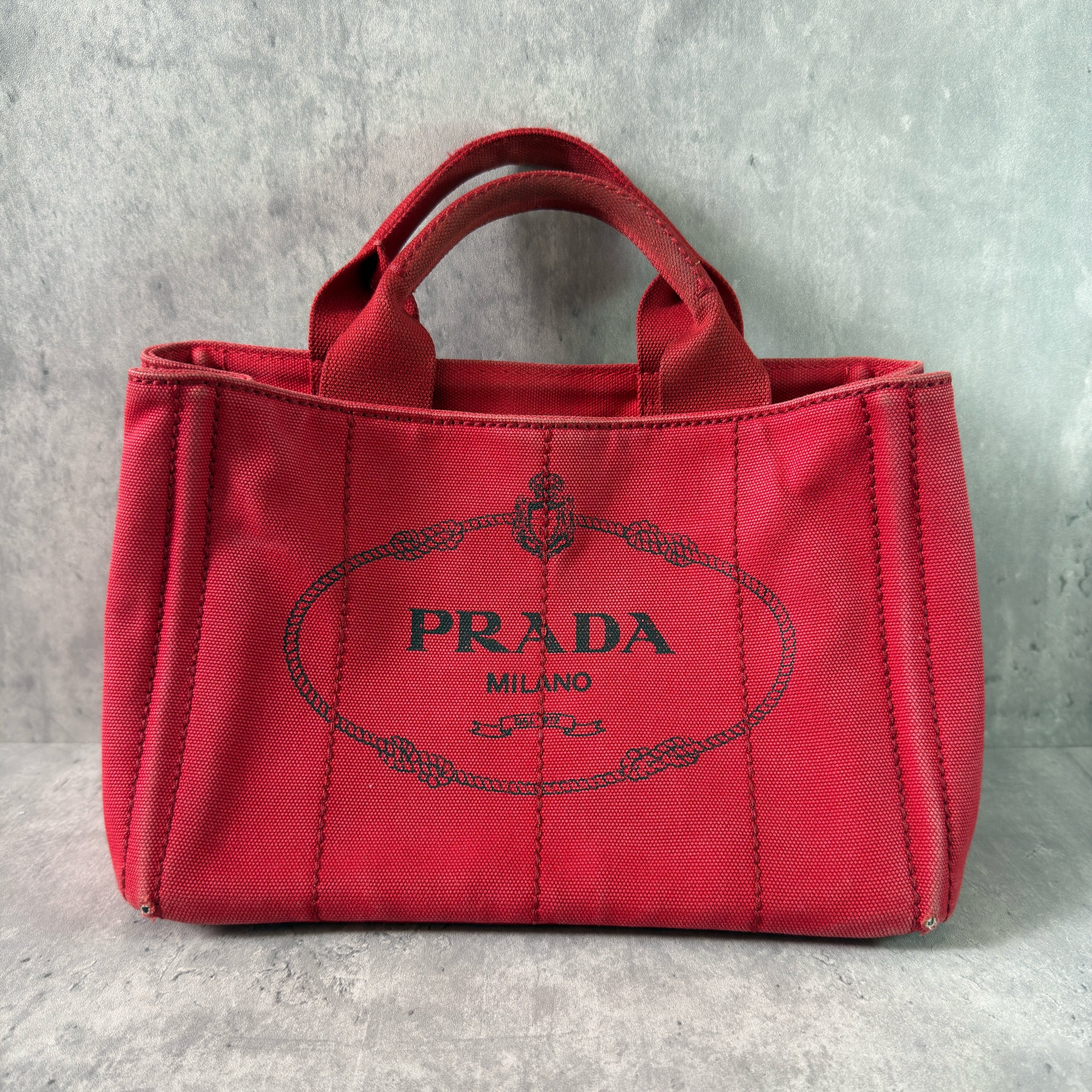 Prada Canapa Tote Bag in red canvas with black logo embroidery, featuring a structured silhouette and dual top handles for effortless style.