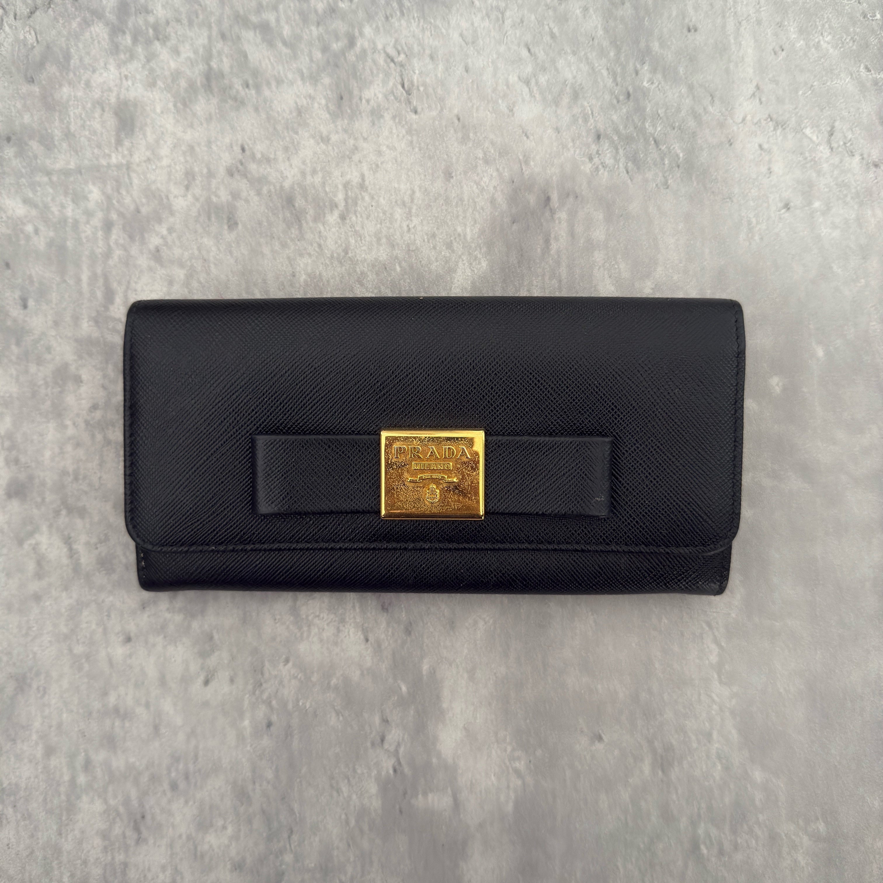 Prada Milano Black Saffiano Leather Ribbon Bow Long Wallet, crafted from textured black Saffiano leather with a gold-tone logo plaque and ribbon bow detail.