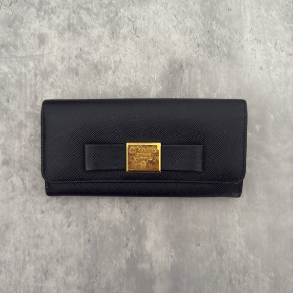 Prada Milano Black Saffiano Leather Ribbon Bow Long Wallet, crafted from textured black Saffiano leather with a gold-tone logo plaque and ribbon bow detail.