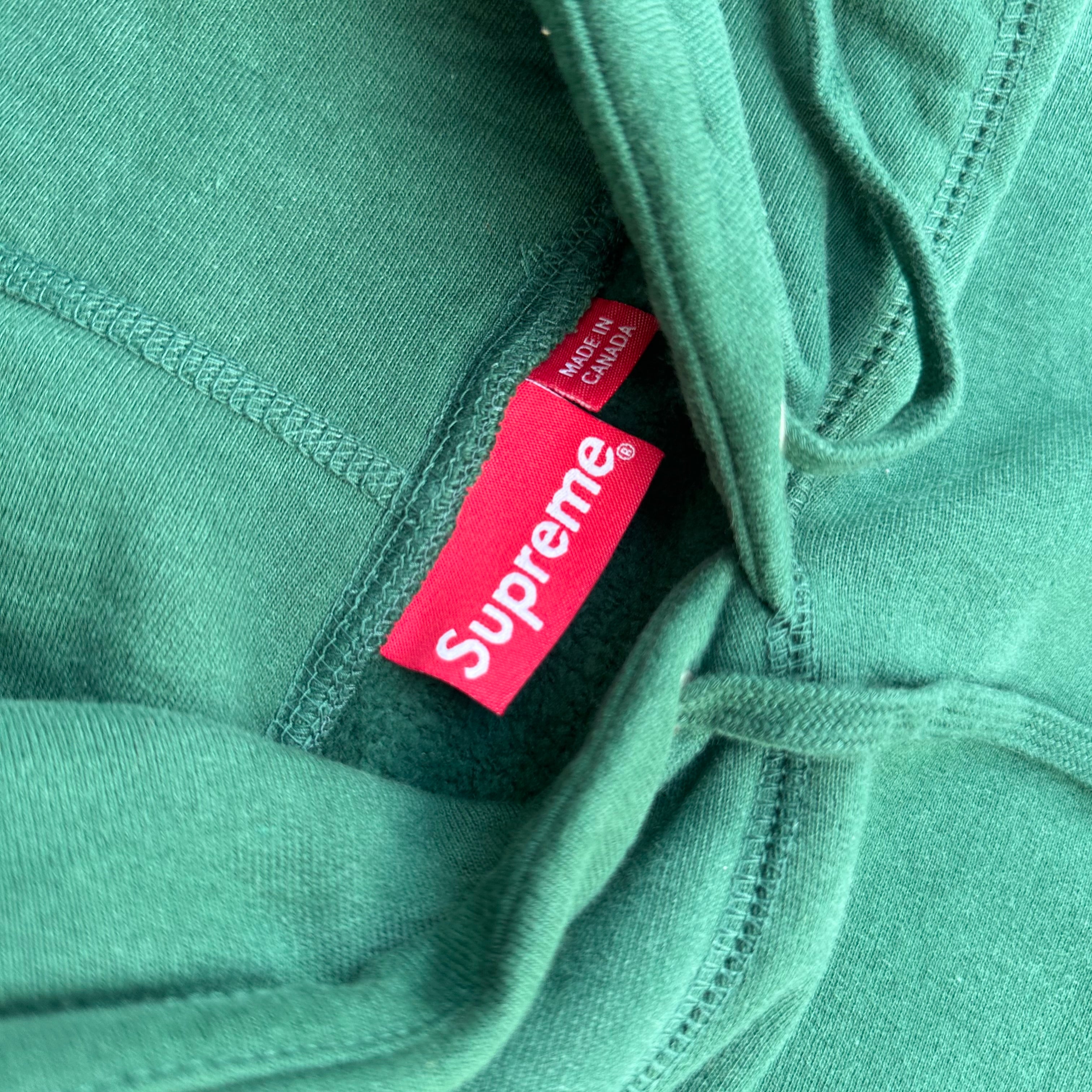 Supreme Arabic Logo Hoodie FW21 in green, featuring orange Arabic logo embroidery and kangaroo pocket, made from heavyweight cotton.
