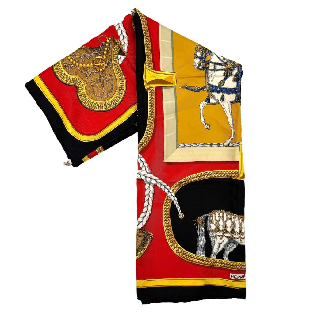 Hermès Grand Apparat silk scarf, featuring an ornate equestrian motif in rich red, gold, and black, elegantly folded to showcase its intricate print.
