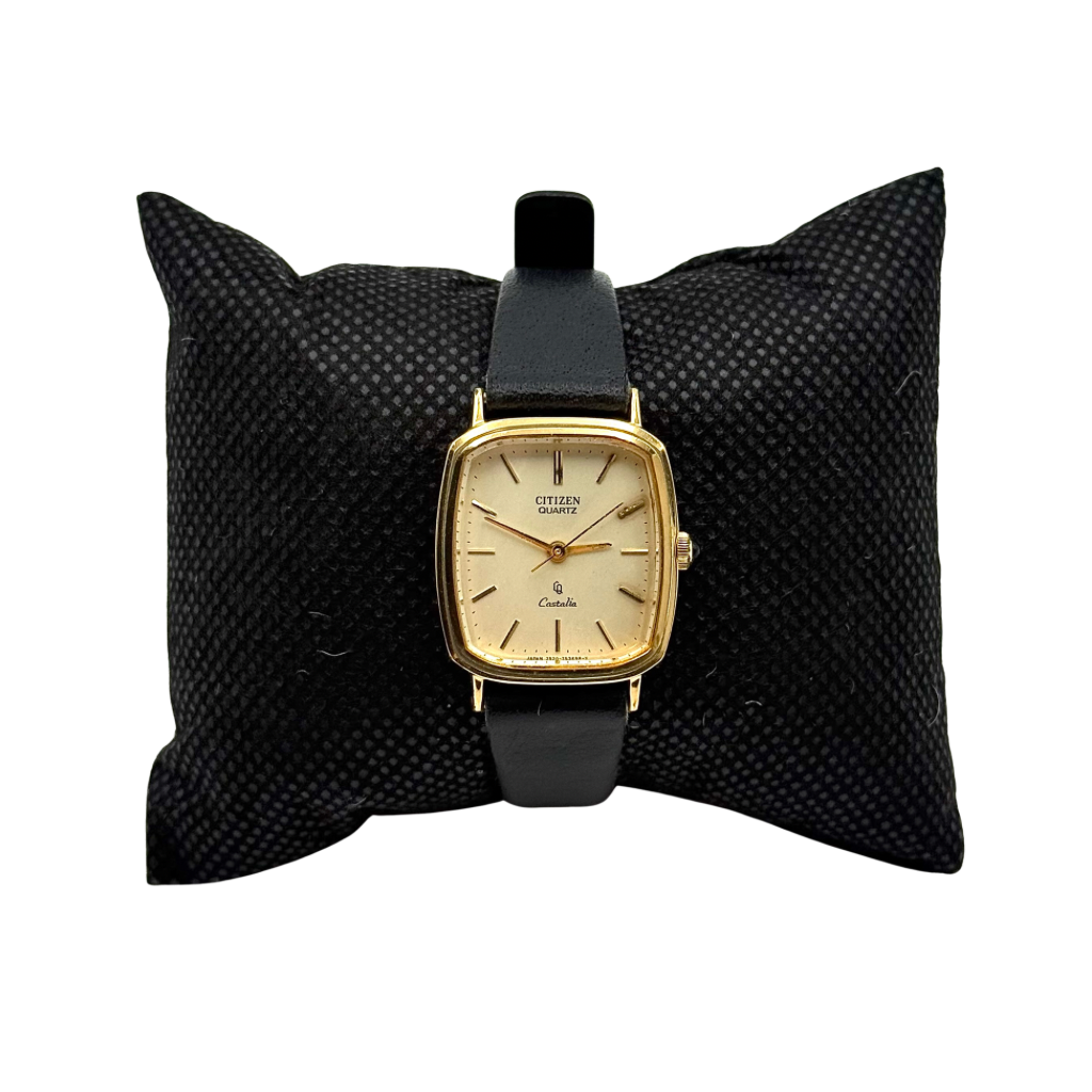 Citizen Castalia gold-tone square quartz watch with a champagne dial and black leather strap displayed on a black cushion.
