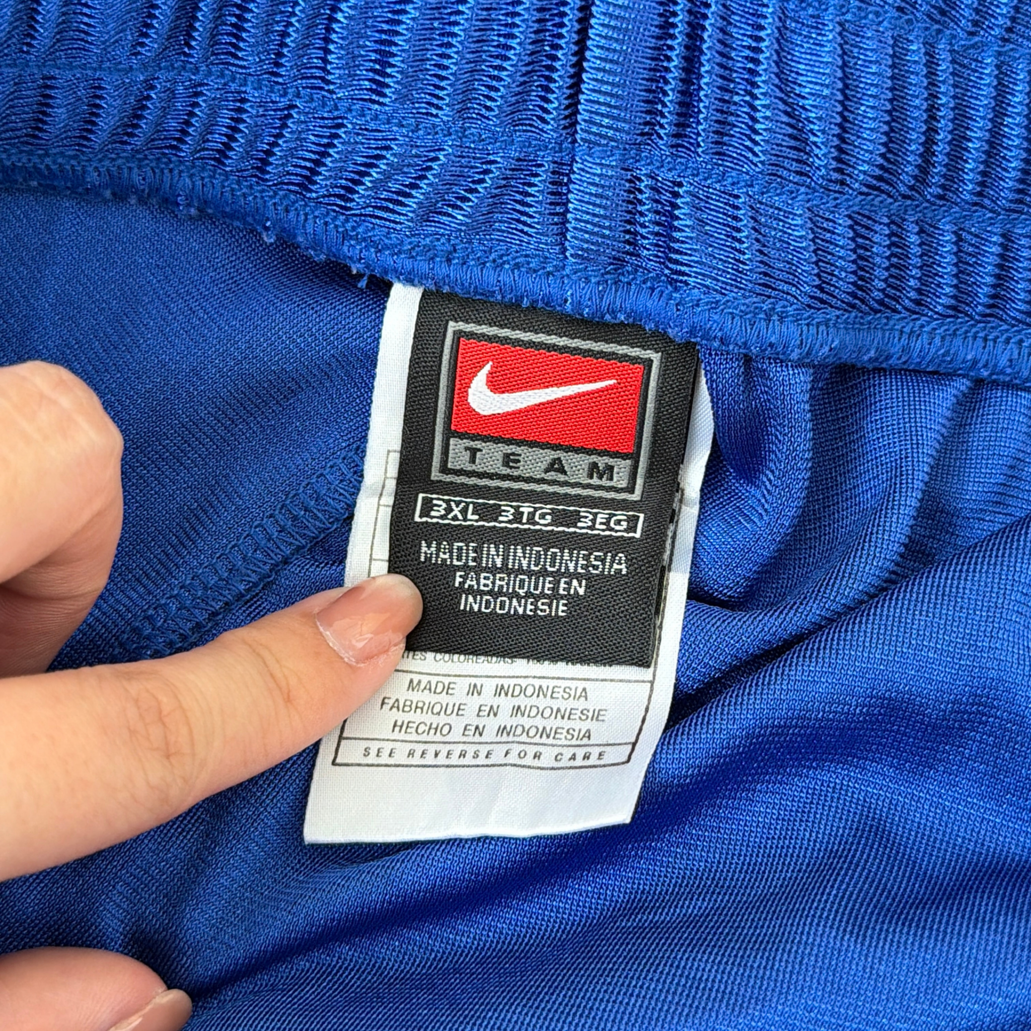 Electric blue Nike tear away track pants with snap button sides and white Swoosh logo displayed flat against a black background.