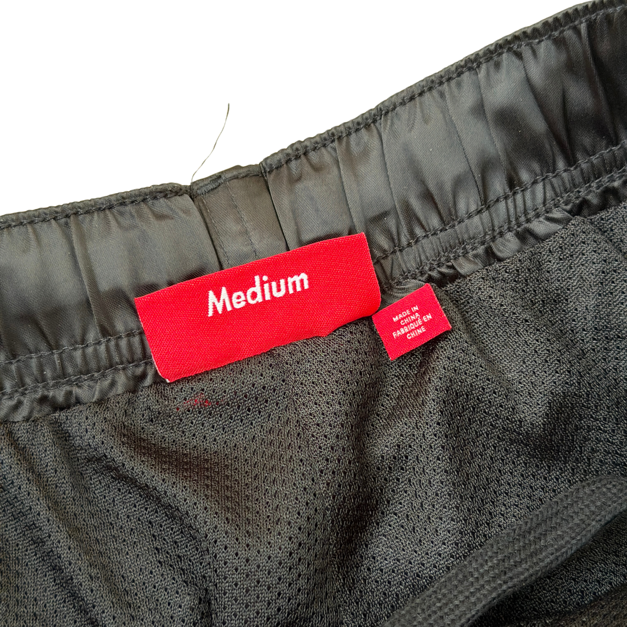 Supreme black satin track pants with white piping, a crest and Supreme logo embroidery at the hip, styled with relaxed legs.