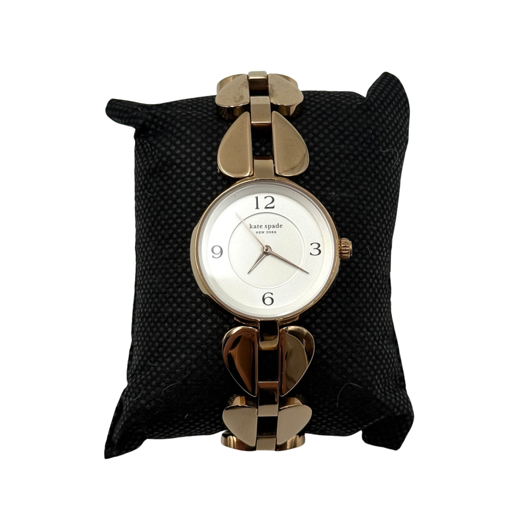 Kate Spade Annadale gold bracelet watch with white dial and heart-shaped links displayed on a black cushion.