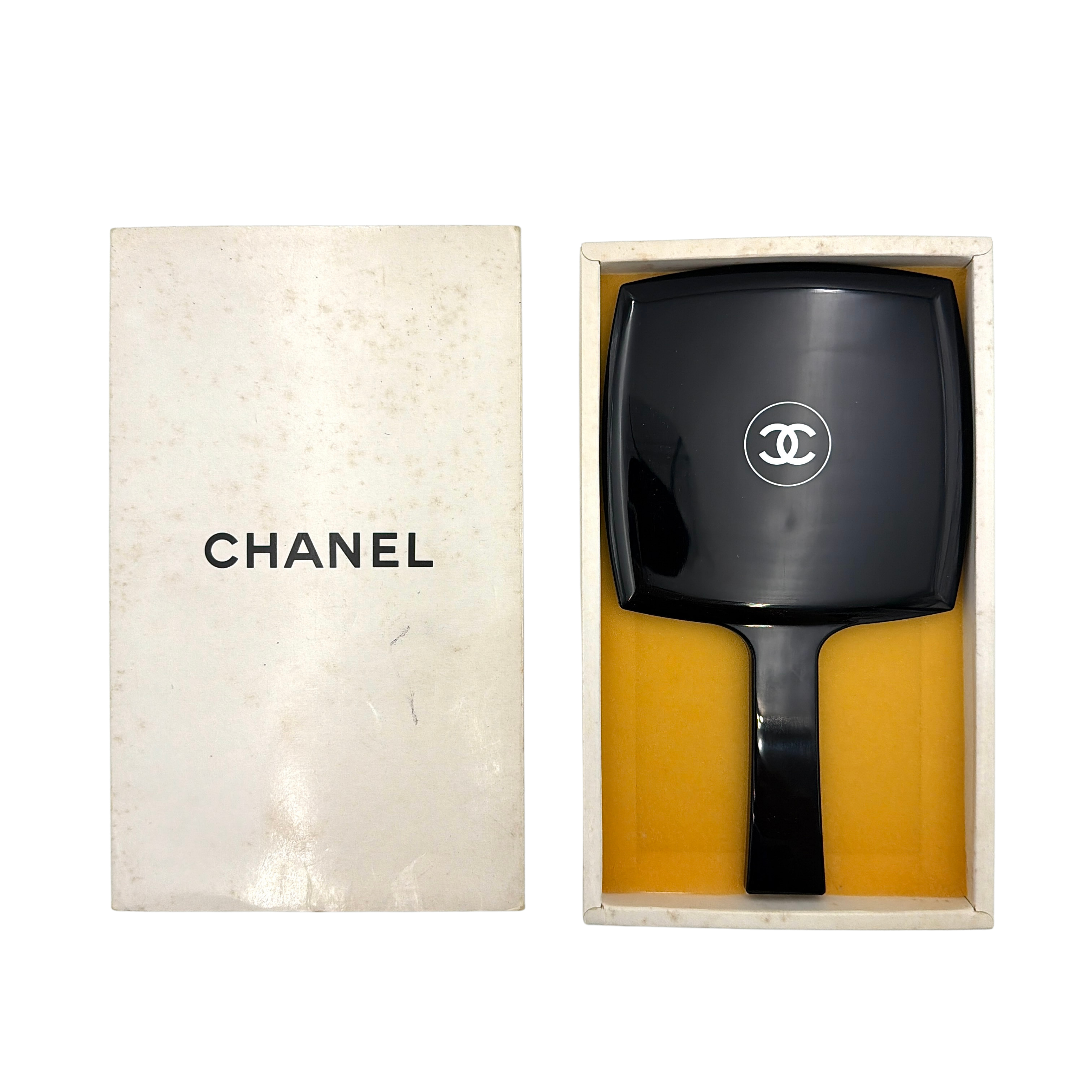 Chanel black hand mirror with white double C logo, presented in its original box with a yellow interior lining.