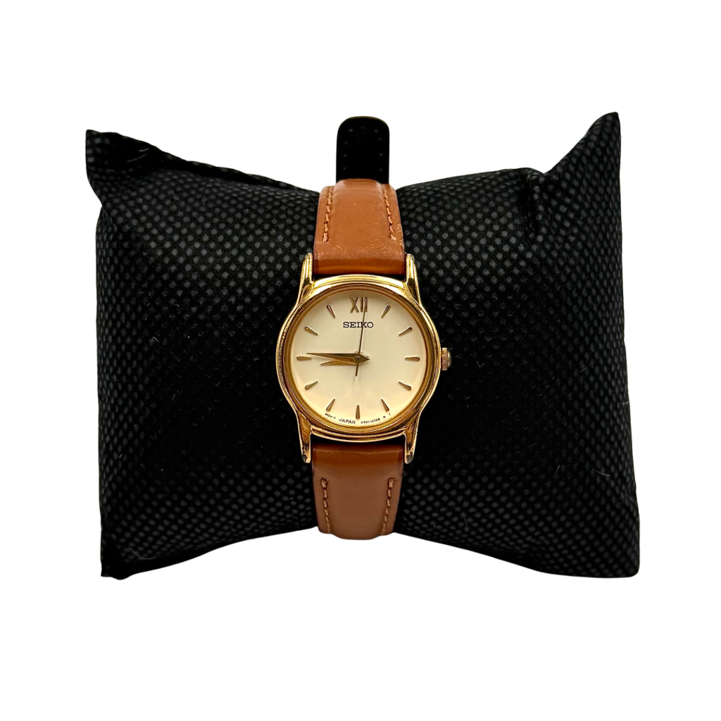 Seiko V701-A110 quartz watch with gold-tone case, cream dial, and brown leather strap on a display pillow.